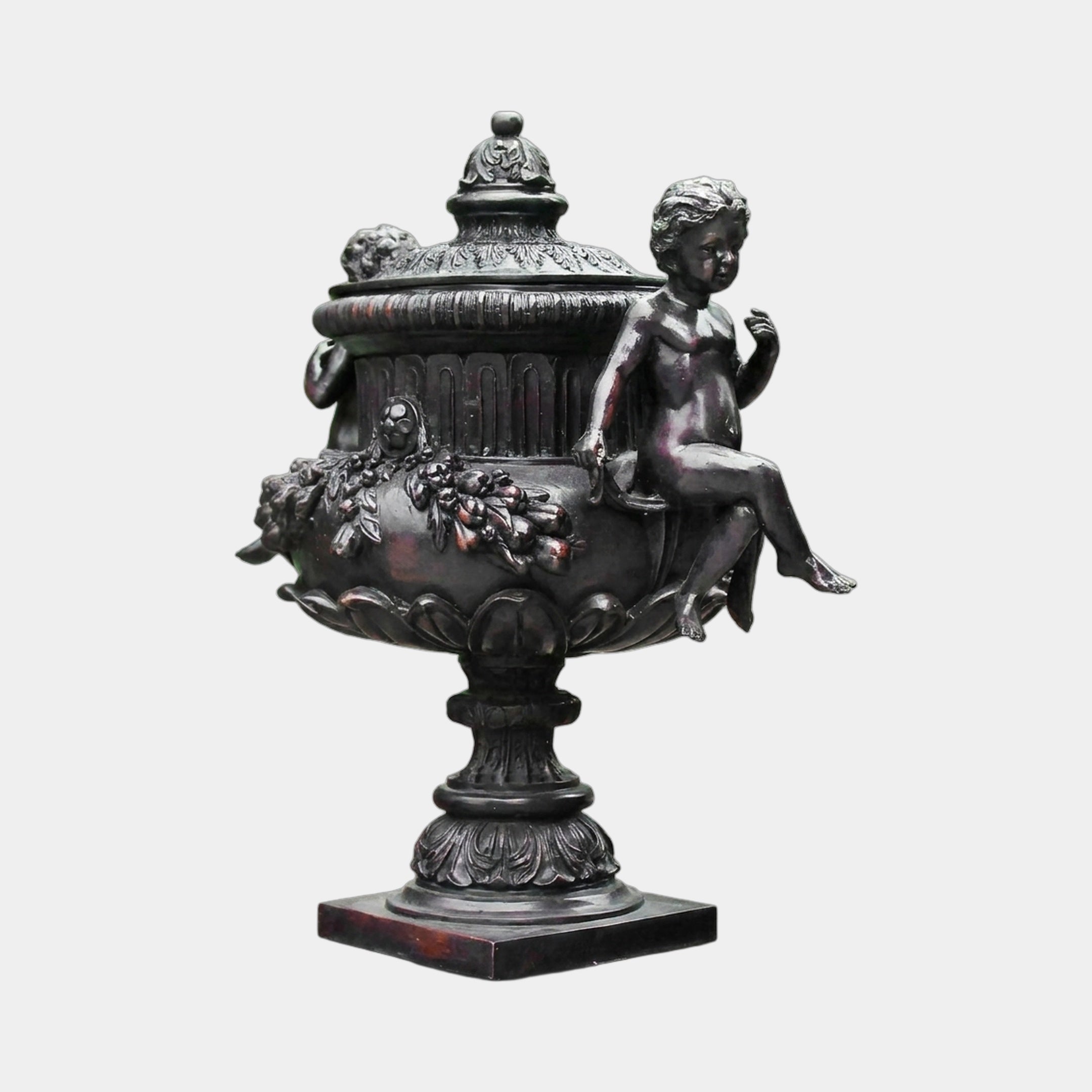 Classical Bronze Cherub Urn Sculpture by Giant Sculptures, 140cm, featuring a seated putto on a garland-decorated urn with domed lid, dark antique patina, plain background.