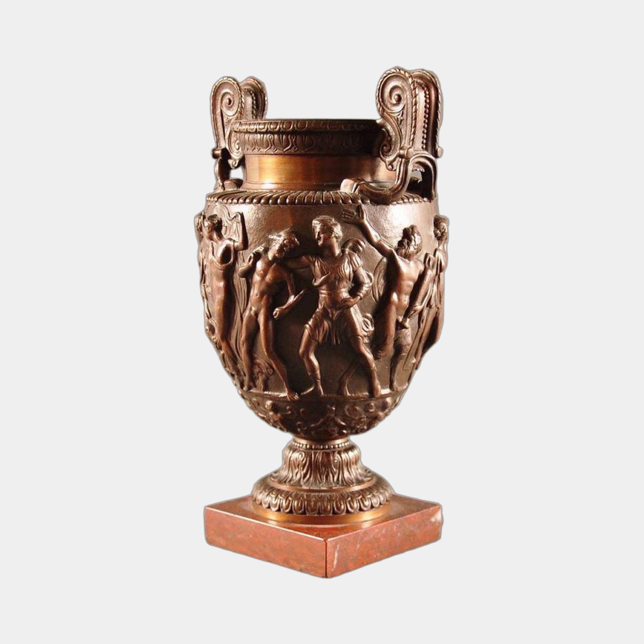 Classical Bronze Urn Vase with Figural Frieze Sculpture by Giant Sculptures, shown with scrolled handles and processional relief on a red marble plinth.