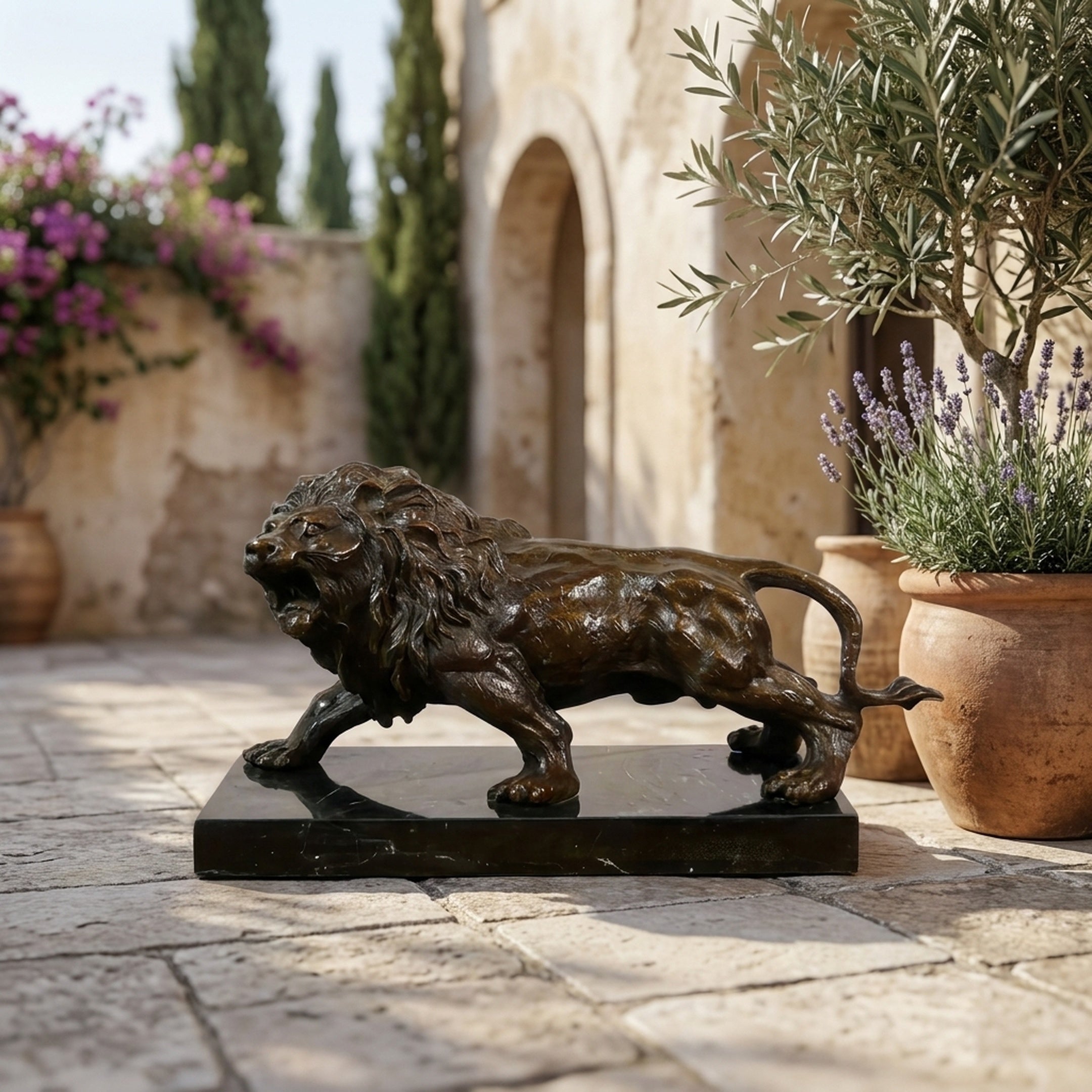 Classical Prowling Lion Bronze Sculpture by Giant Sculptures on a black marble base, displayed on a Mediterranean stone courtyard beside potted olive and lavender.