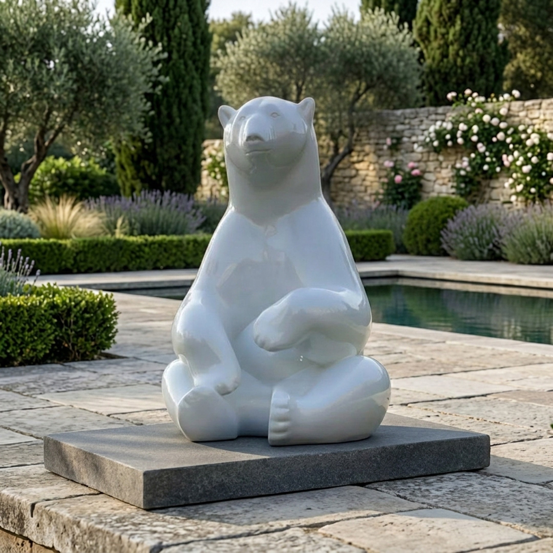 Giant Contemporary Polar Bear Bronze Sculpture by Giant Sculptures in glossy white, seated upright on a black plinth beside a garden pool with lavender.