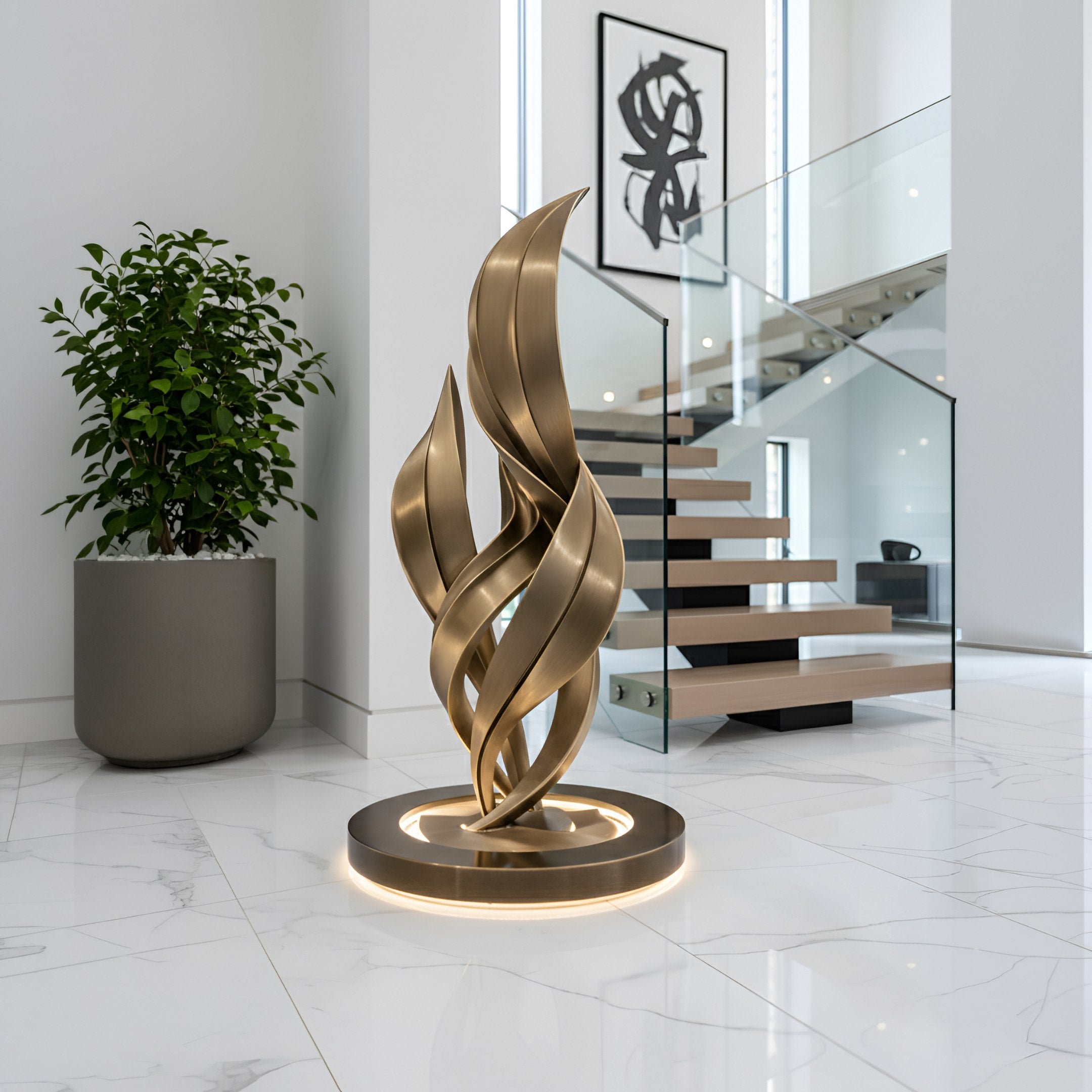 The Ignite Bronze Abstract Steel Sculpture (220cm) by Giant Sculptures features gold, flame-like ribbons and built-in lighting on a circular base, displayed in a bright, minimalist room with marble floors, a potted plant, and glass-railed stairs.