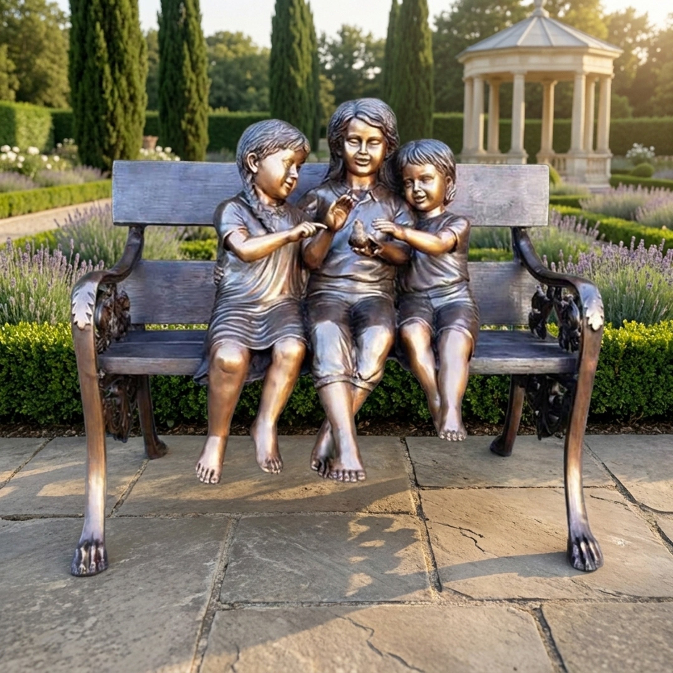 Large Traditional Children on Bench Bronze Sculpture by Giant Sculptures, three barefoot children seated together holding a bird, in a lavender garden.