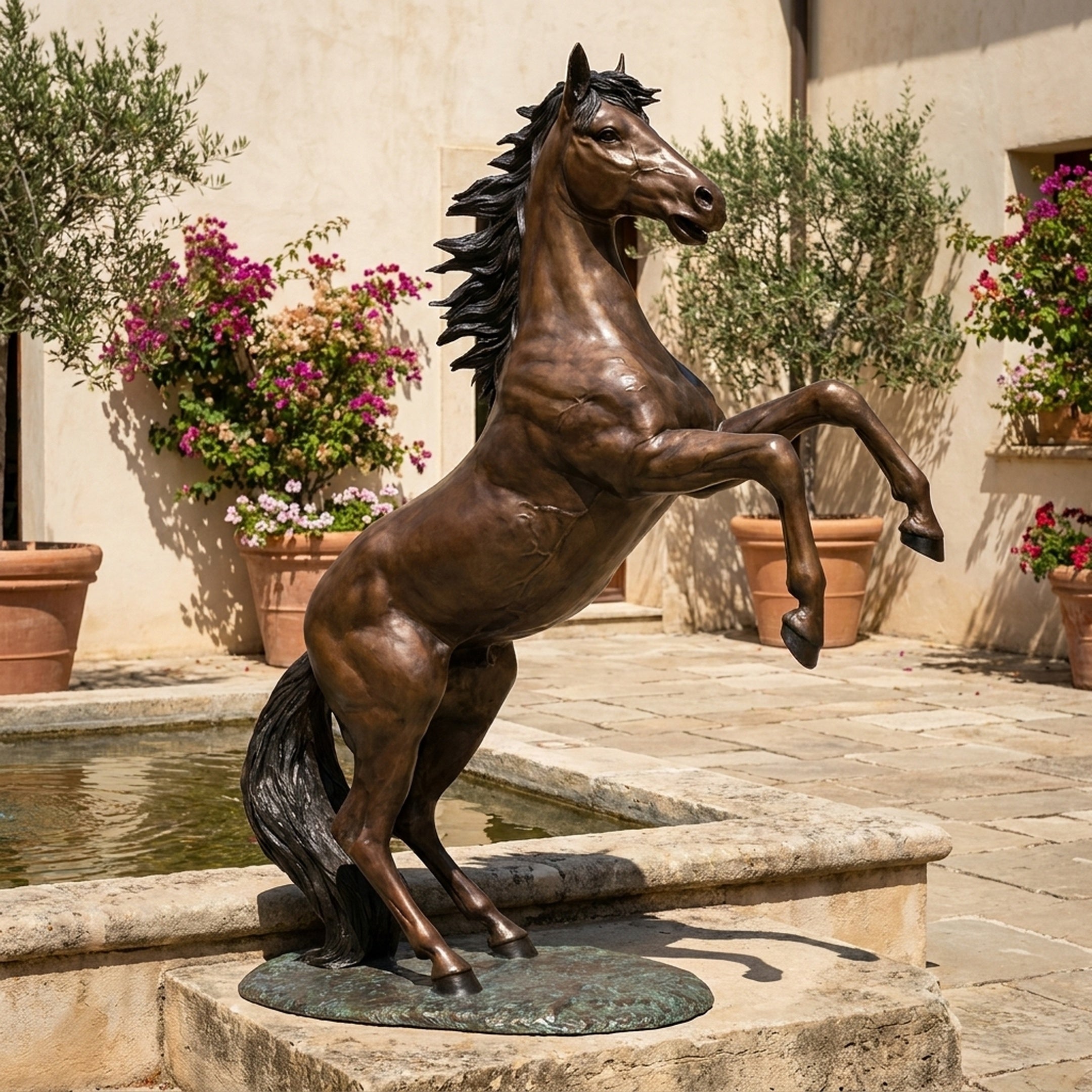 Life-Size Classical Rearing Horse Bronze Sculpture by Giant Sculptures, shown rearing on a stone fountain edge in a Mediterranean courtyard with potted bougainvillea.