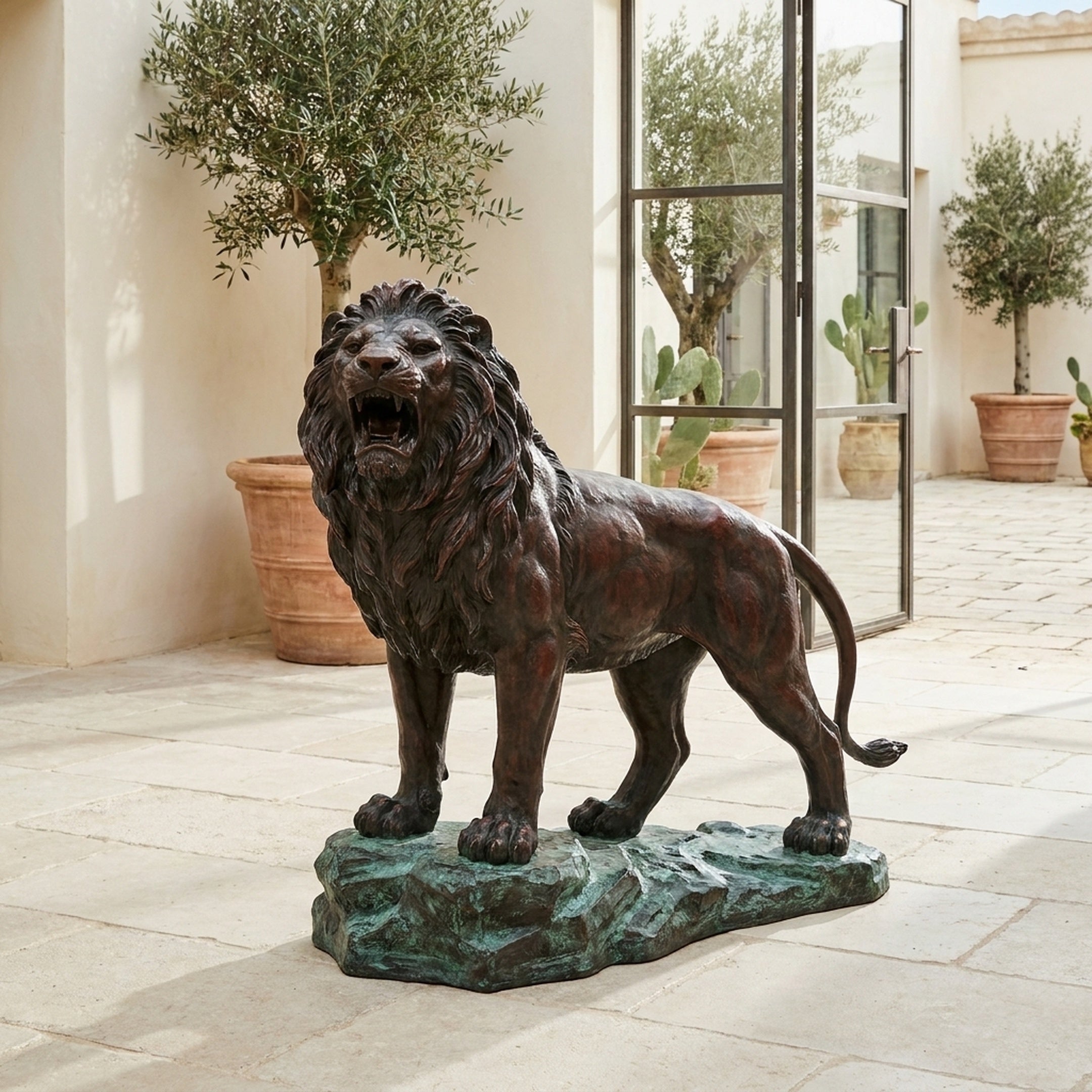 Giant Sculptures Life-Size Classical Roaring Male Lion Bronze Sculpture on a verdigris rocky base, displayed in a Mediterranean courtyard with olive trees.