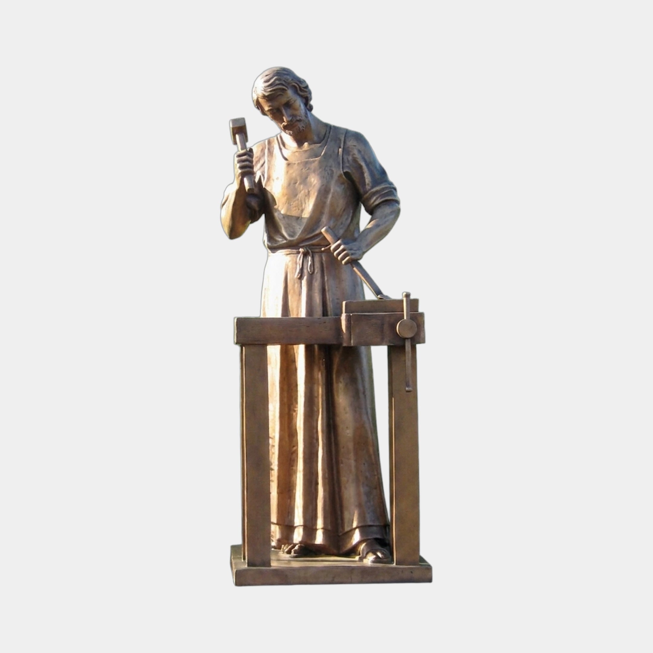 Life-Size Classical Saint Joseph the Worker Bronze Sculpture by Giant Sculptures, robed figure raising a mallet at a carpenter's workbench, warm golden-brown patina.