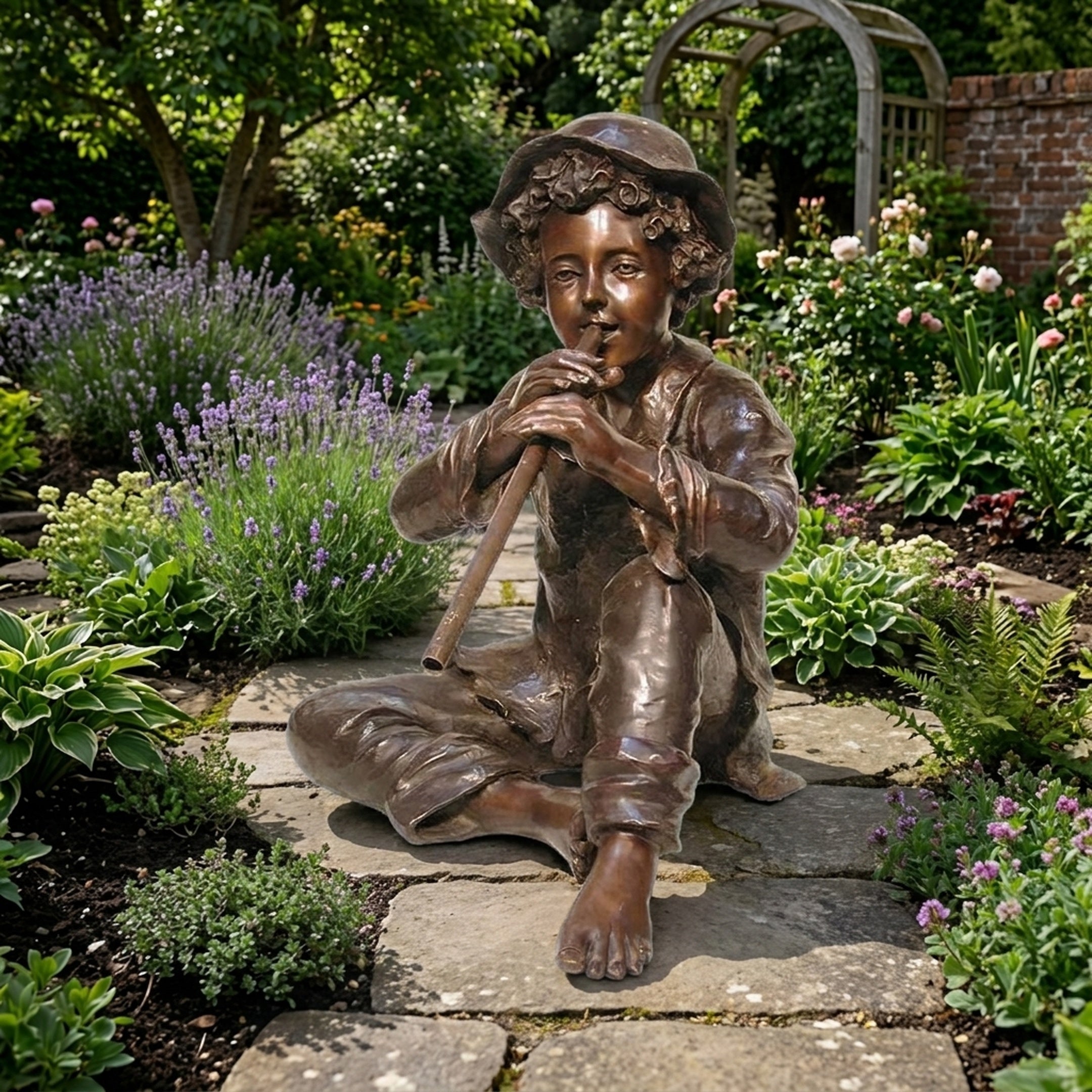 Life-Size Classical Seated Boy Playing Flute Bronze Sculpture by Giant Sculptures, shown barefoot and cross-legged on a stone path among lavender and roses.