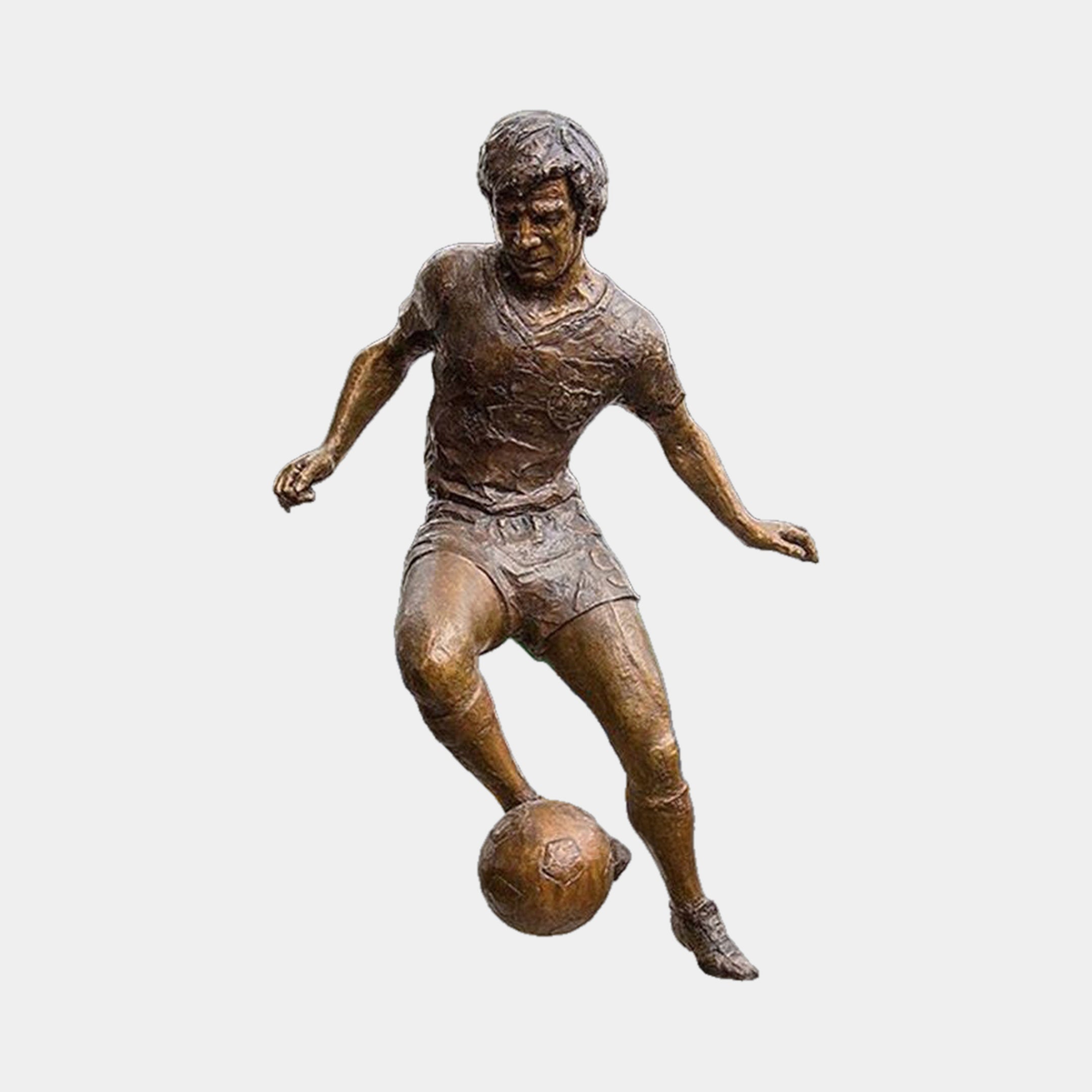 Life-Size Contemporary Footballer Dribbling Bronze Sculpture by Giant Sculptures in mid-brown patina, mid-stride with right boot to the ball, on a plain background.