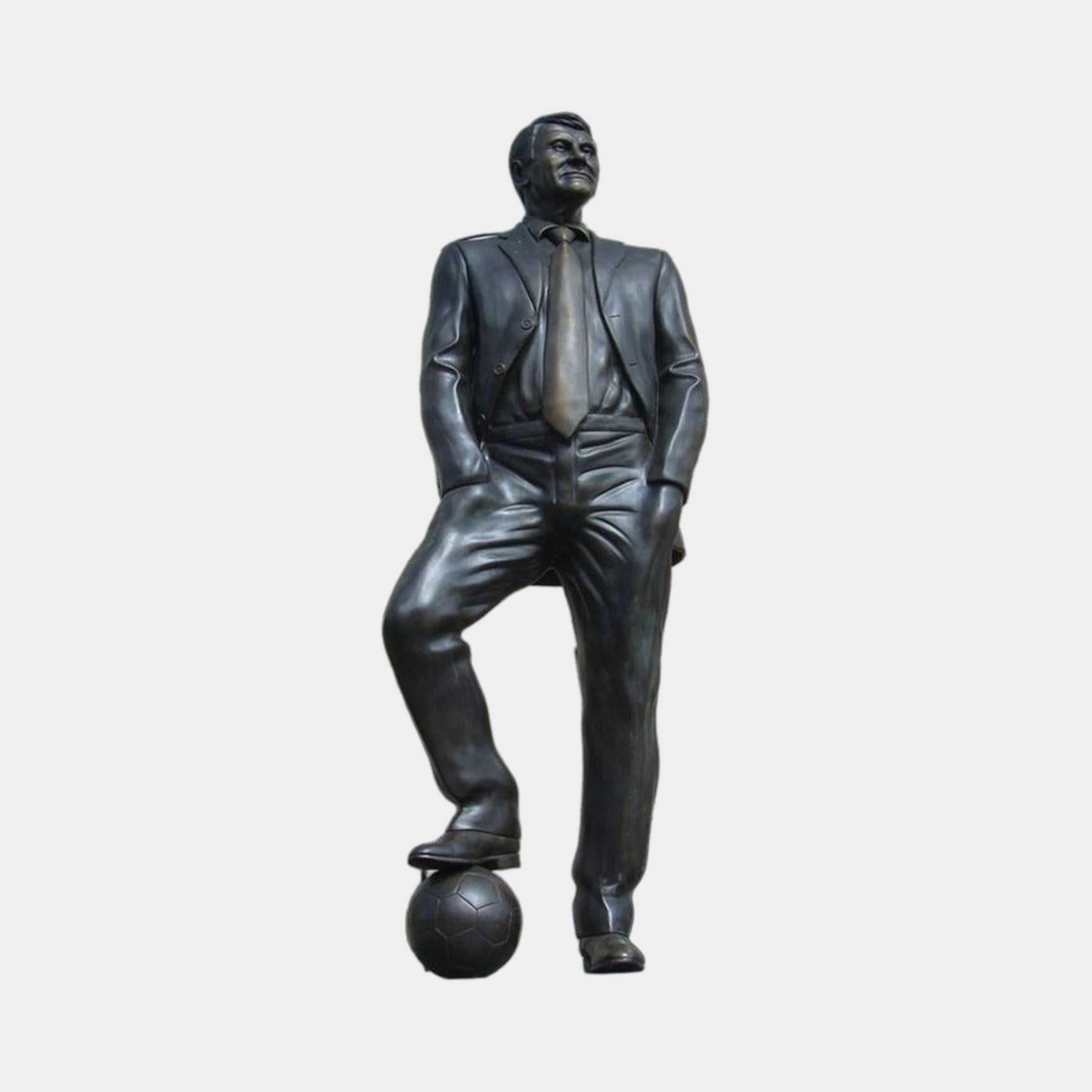 Life-Size Contemporary Male Figure Bronze Sculpture by Giant Sculptures, 290cm dark-patina suited man with one foot resting on a football, on plain background.
