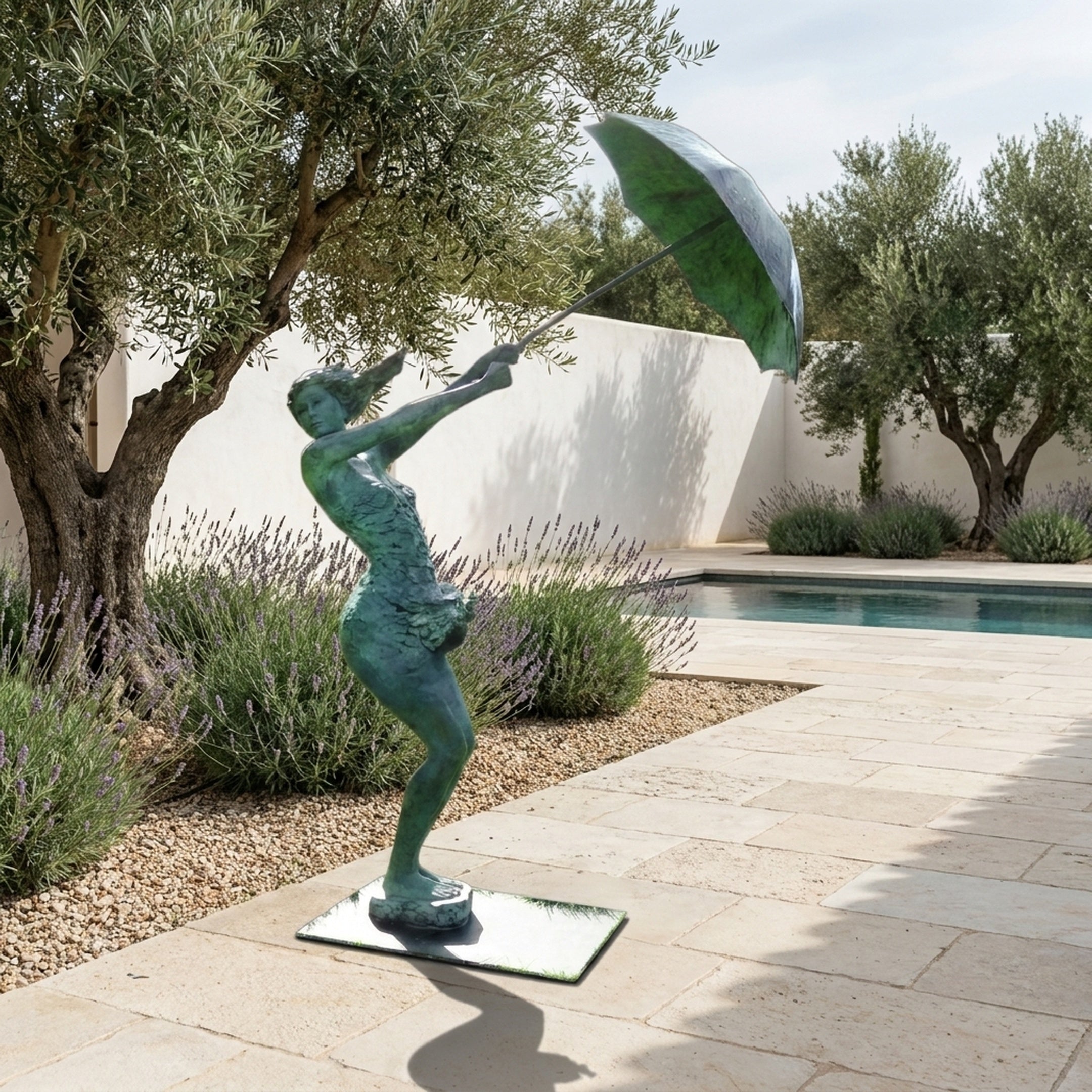 Life-Size Contemporary Windswept Woman with Umbrella Bronze Sculpture in verdigris finish, displayed on a poolside terrace with olive trees and lavender.