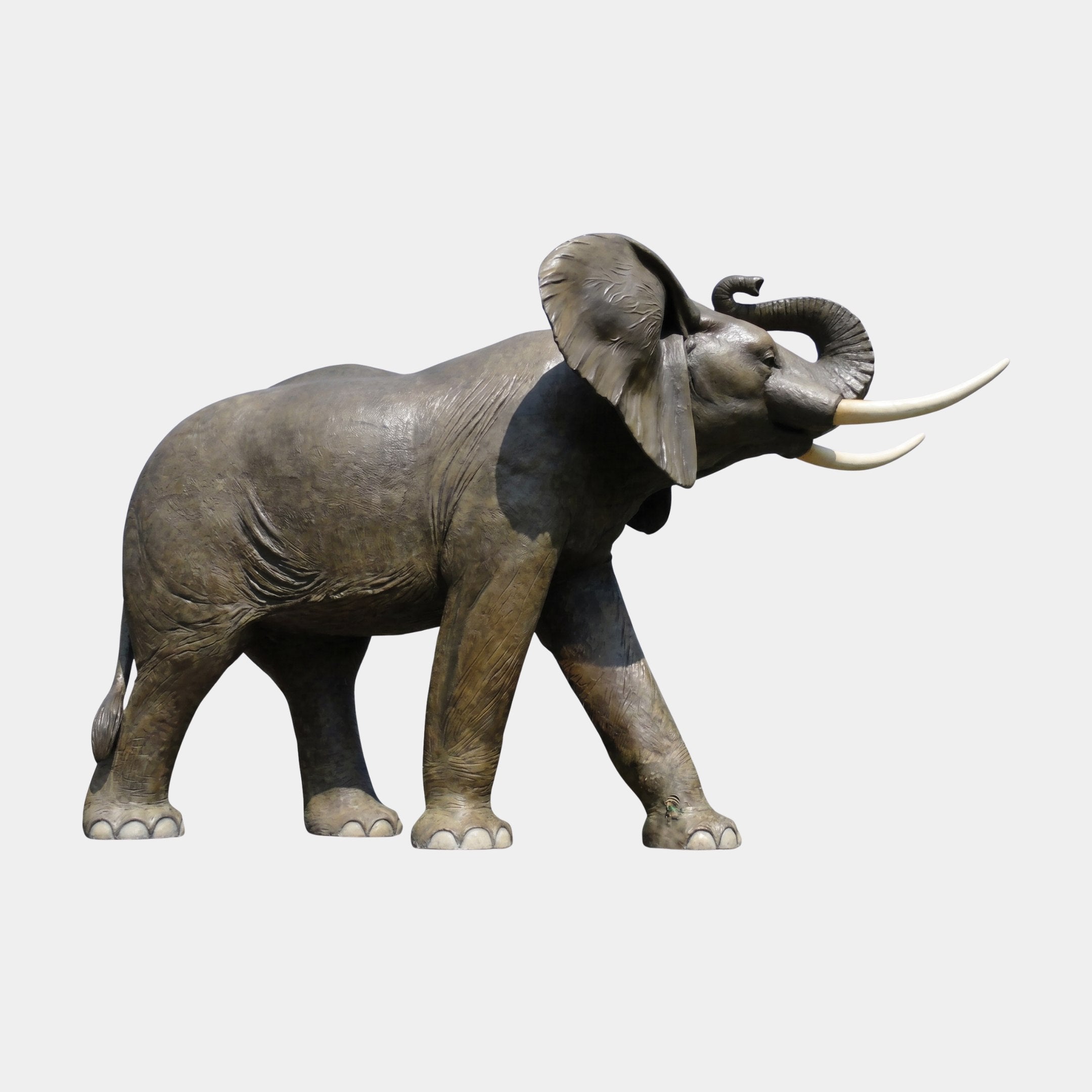 Life-Size Traditional African Elephant Bronze Sculpture by Giant Sculptures, side view with raised trunk, ivory tusks, and warm brown patina on a plain background.