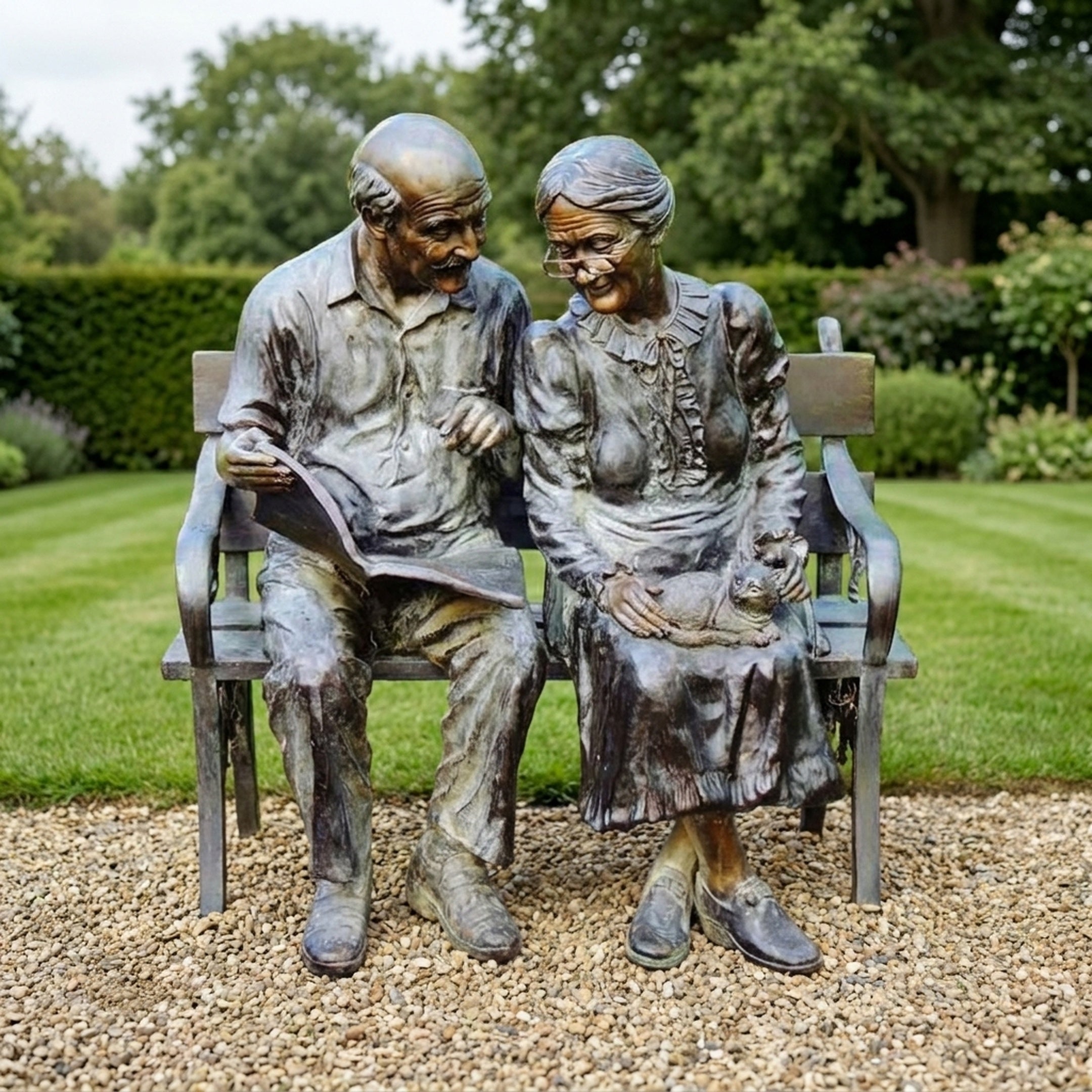 Life-Size Traditional Elderly Couple on Bench Bronze Sculpture by Giant Sculptures, seated together on a garden path with a book and a cat in her lap.