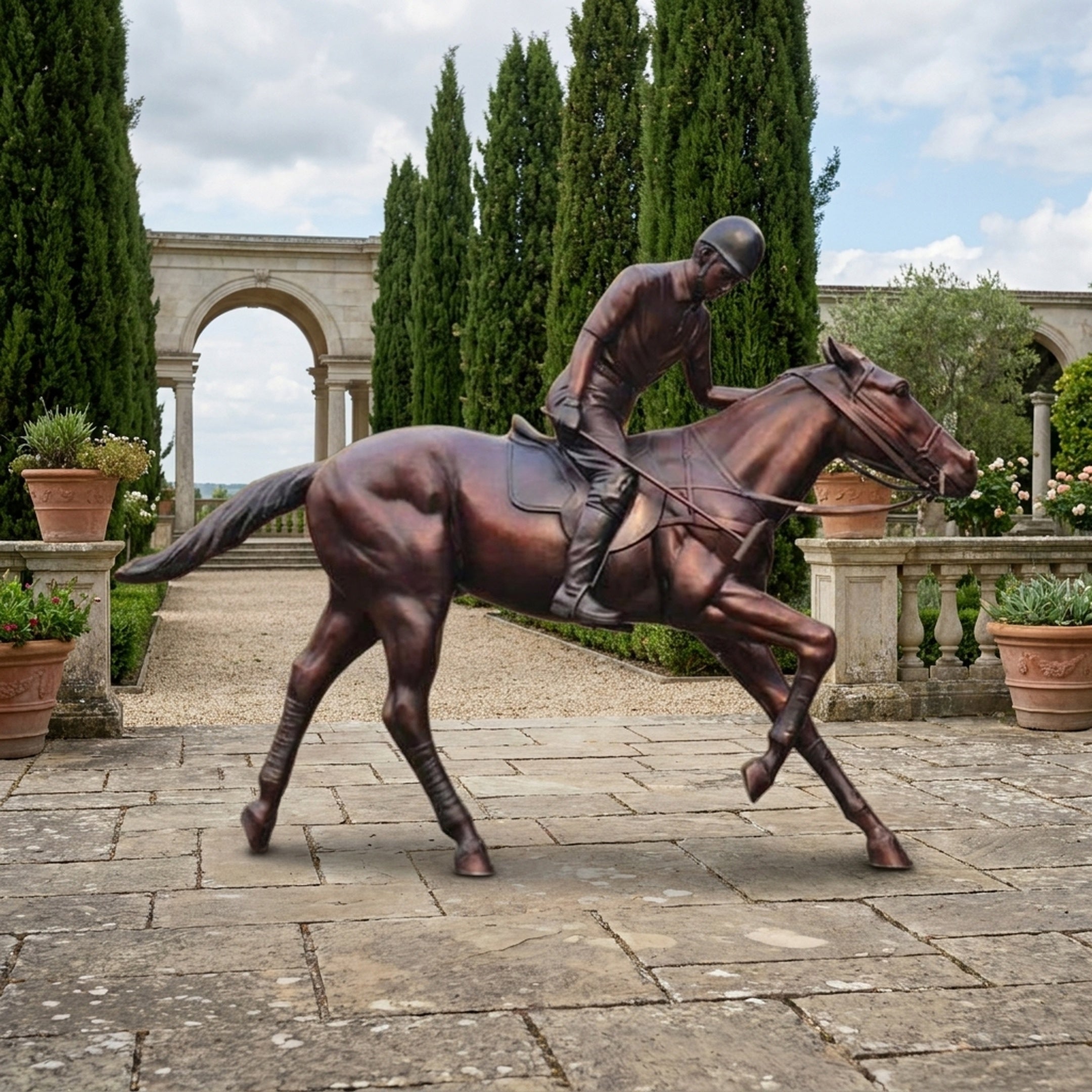 Life-Size Traditional Jockey and Galloping Horse Bronze Sculpture by Giant Sculptures displayed on a stone terrace with cypress trees and a classical archway.