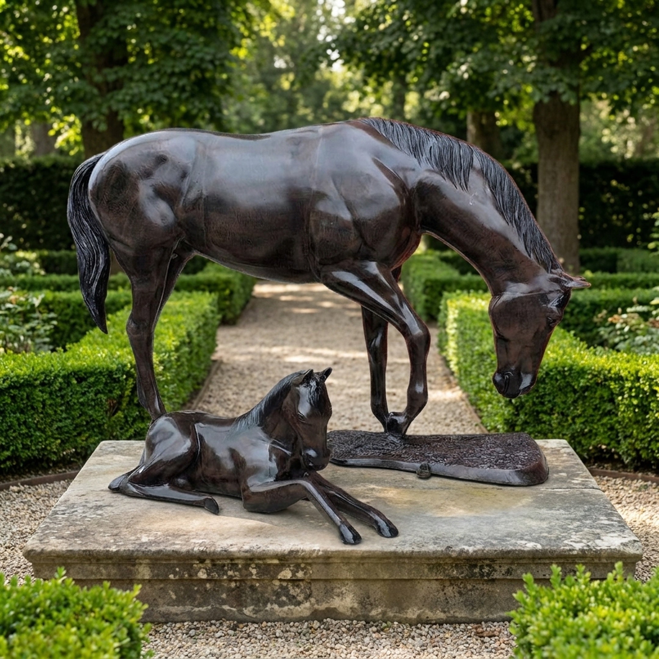 Life-Size Traditional Mare and Foal Bronze Sculpture by Giant Sculptures, dark brown patina, displayed on a stone plinth in a hedged garden pathway.