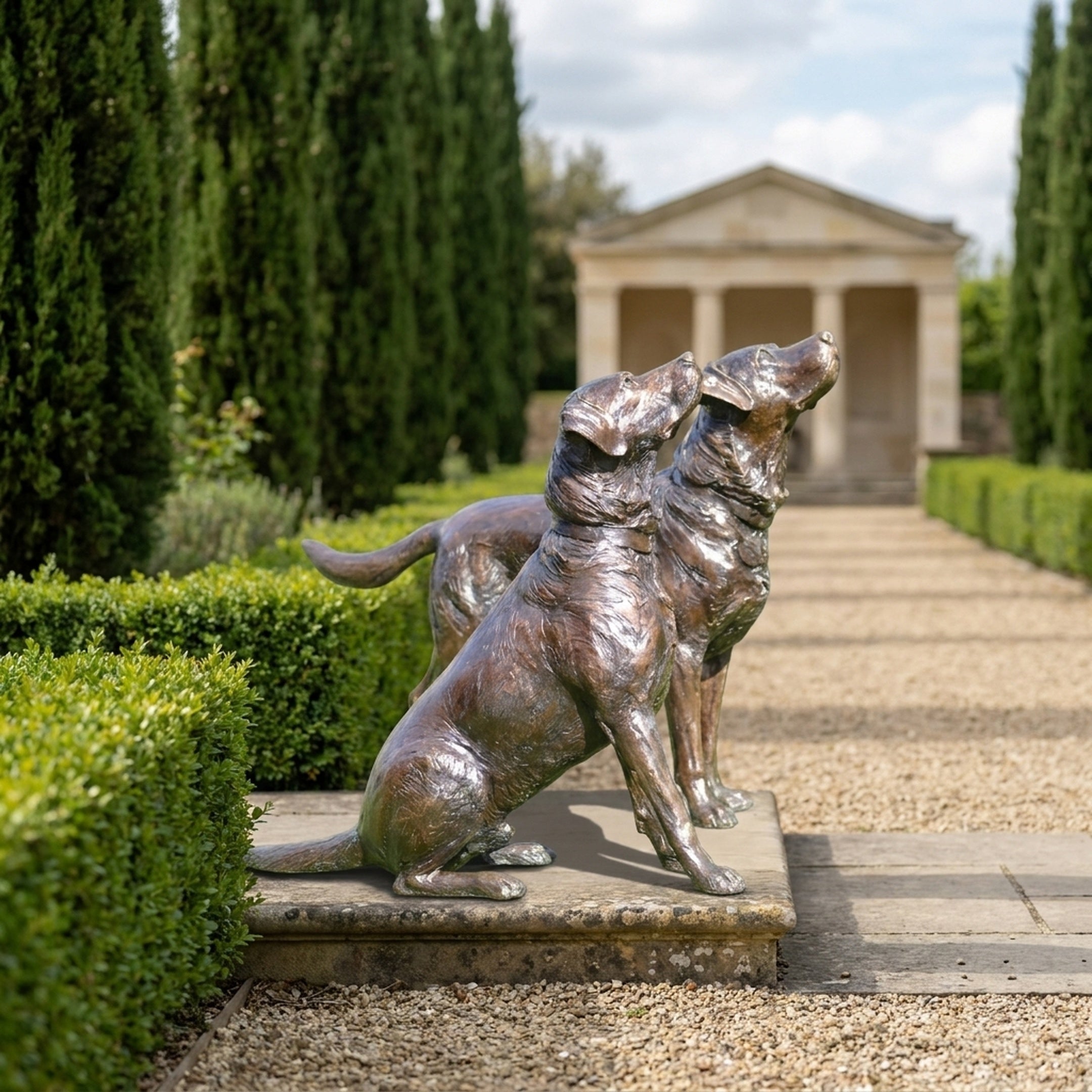 Life-Size Traditional Paired Labradors Bronze Sculpture by Giant Sculptures displayed on a stone plinth along a gravel path lined with cypress trees.