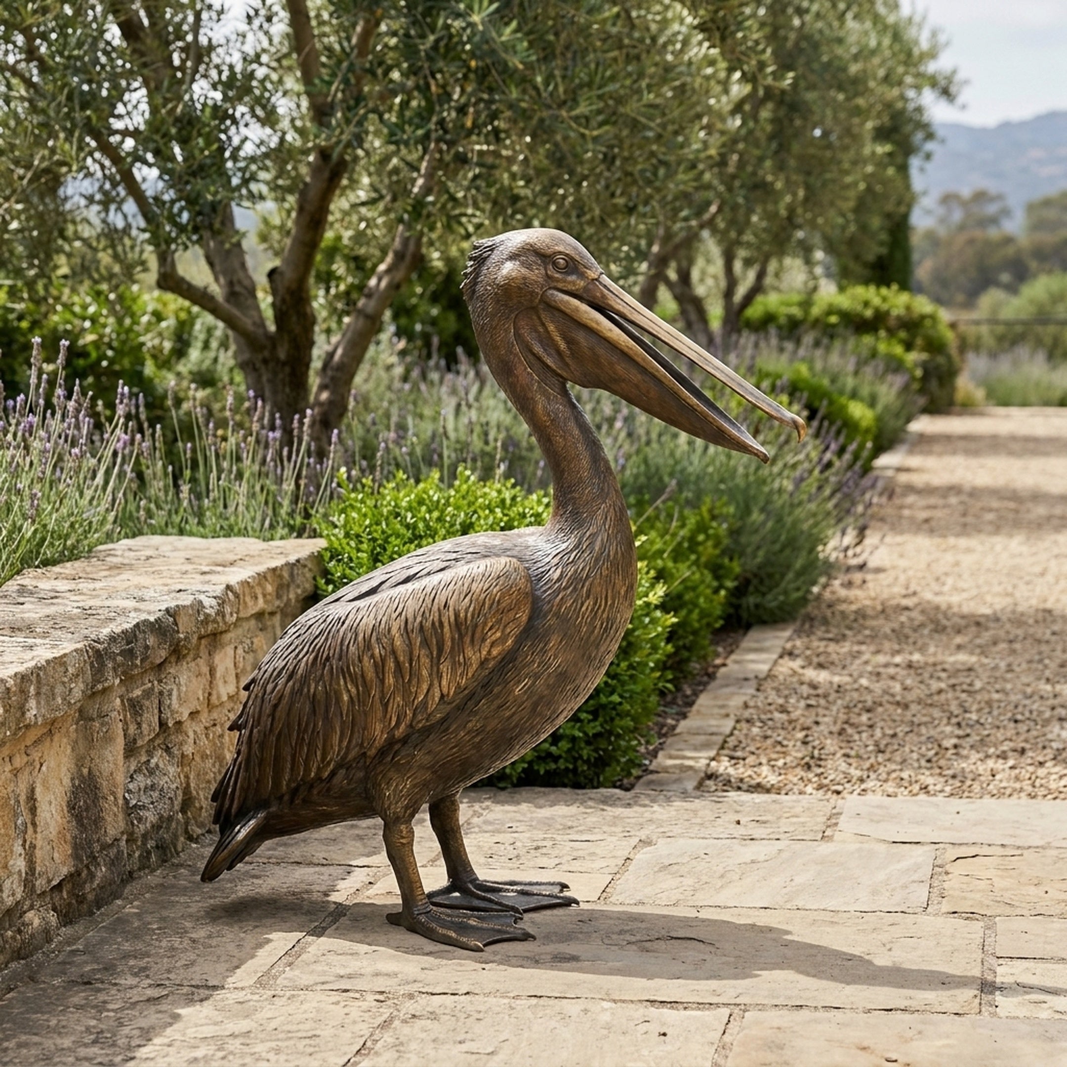 Life-Size Traditional Pelican Bronze Sculpture by Giant Sculptures shown in side profile on a stone terrace beside lavender and olive trees, beak open.