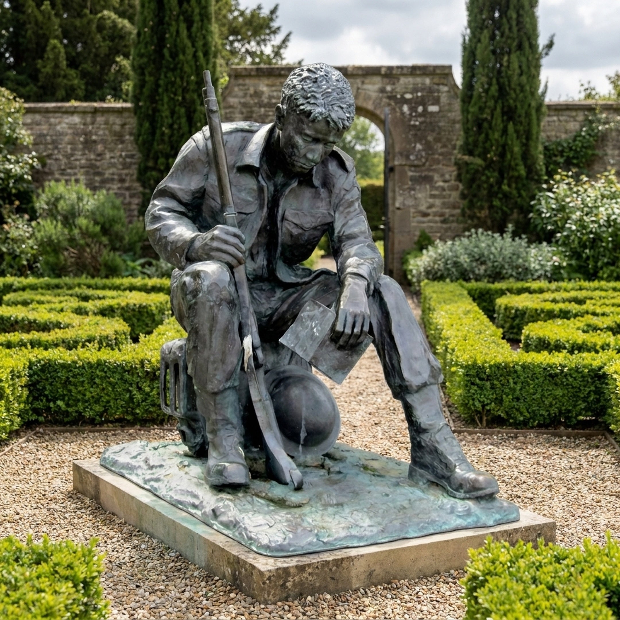 Giant Sculptures Life-Size Traditional Seated Soldier Bronze Sculpture with head bowed, holding a rifle and helmet, on a granite plinth in a hedged garden.