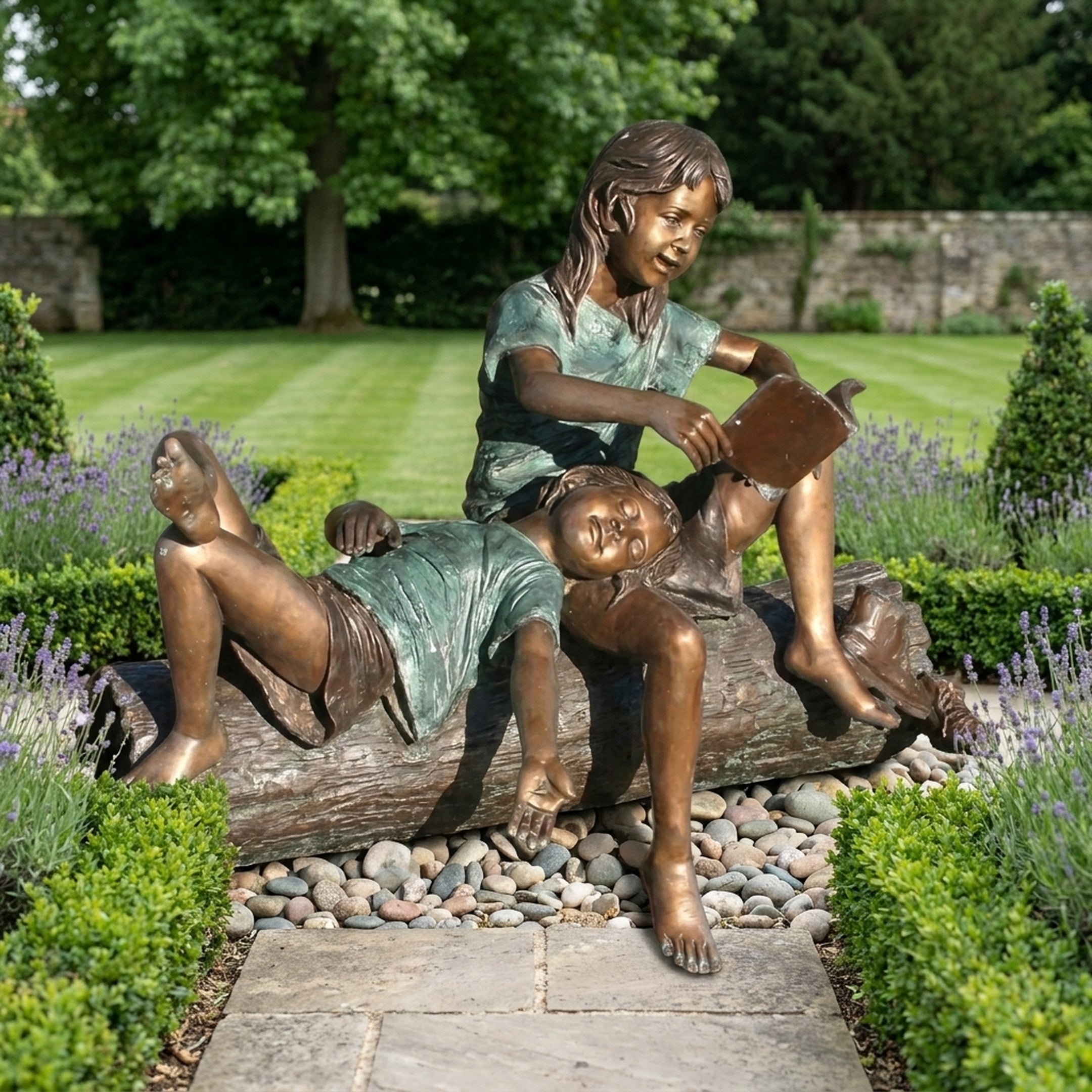 Life-Size Traditional Two Children Bronze Sculpture by Giant Sculptures on a log, older girl reading aloud while a younger child reclines across her lap in a garden.