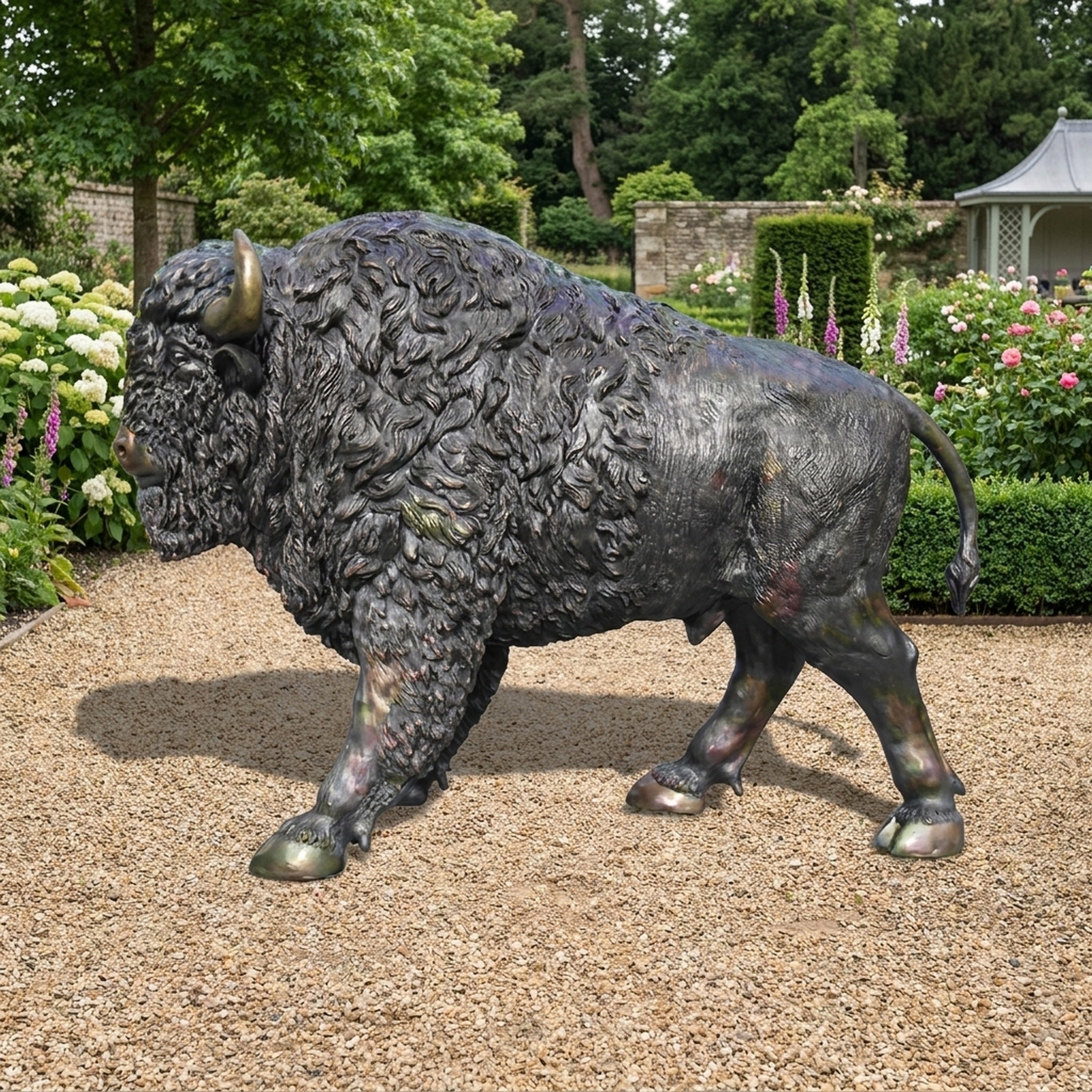Life-Size Traditional Walking Bison Bronze Sculpture by Giant Sculptures shown in mid-stride on a gravel garden path with hydrangeas and roses behind.