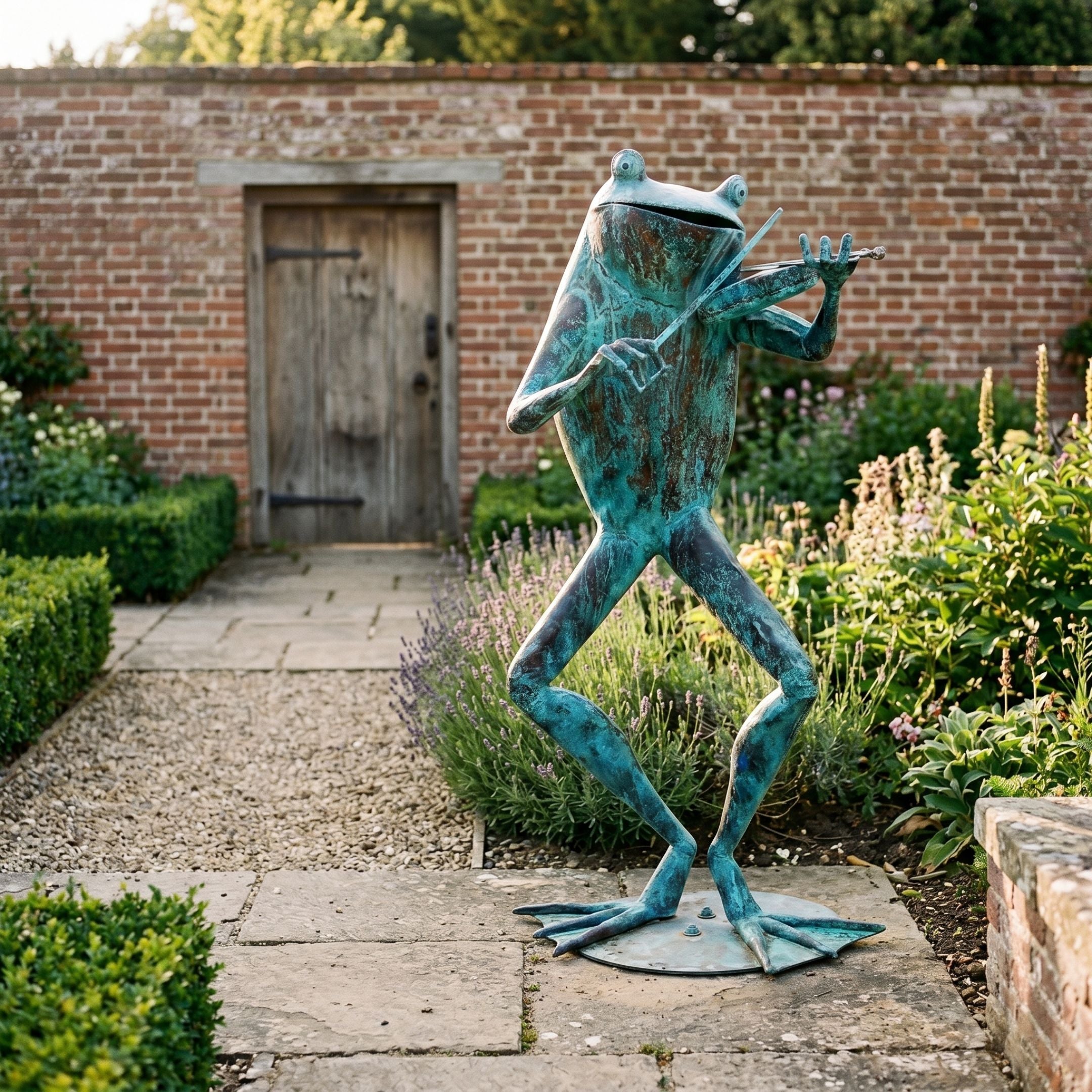 Monumental Flute-Playing Frog Bronze Sculpture by Giant Sculptures with verdigris patina, standing on a stone path beside lavender in a walled garden.