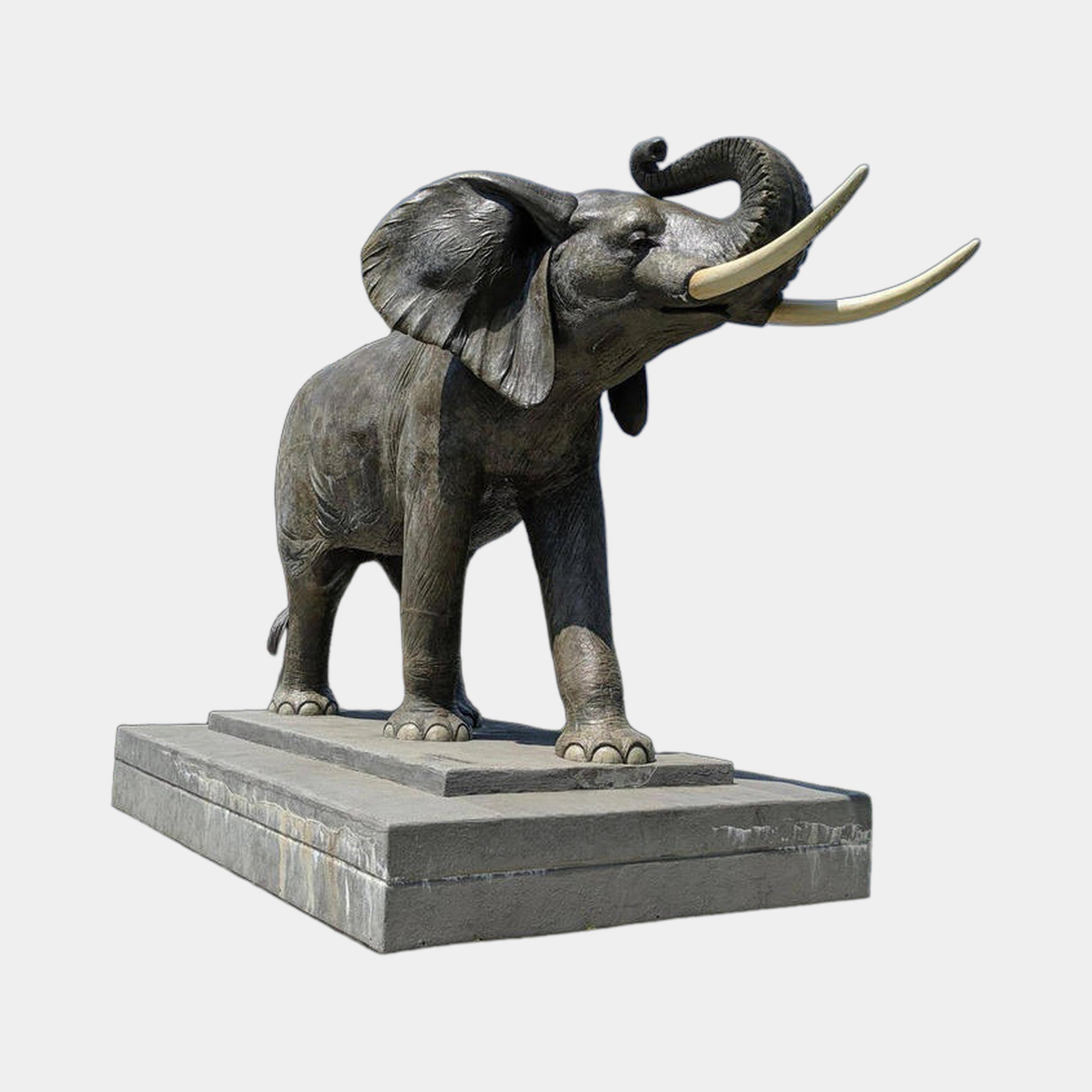 Giant Sculptures Monumental Traditional Bull Elephant Bronze Sculpture 360cm, trunk raised with pale cream tusks, on a two-tiered stone plinth against grey.