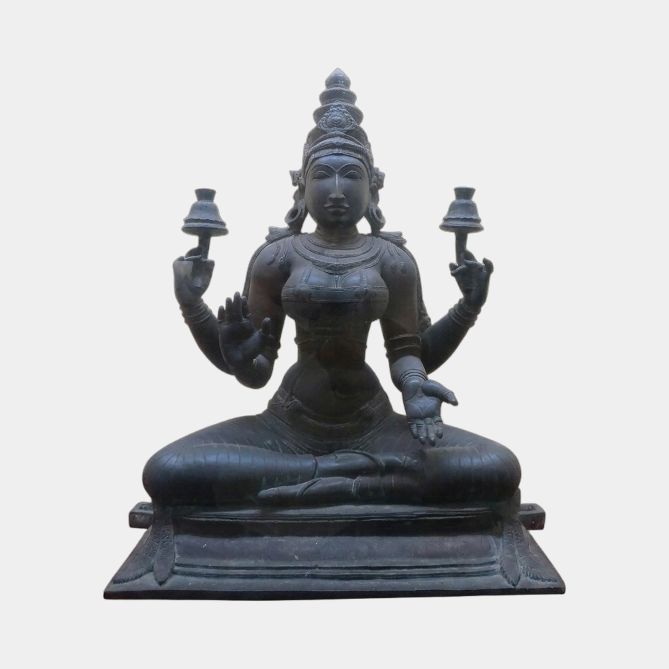 Monumental Traditional Four-Armed Goddess Bronze Statue by Giant Sculptures, seated in padmasana with dark patina, holding lamps and varada-abhaya mudras, on white.