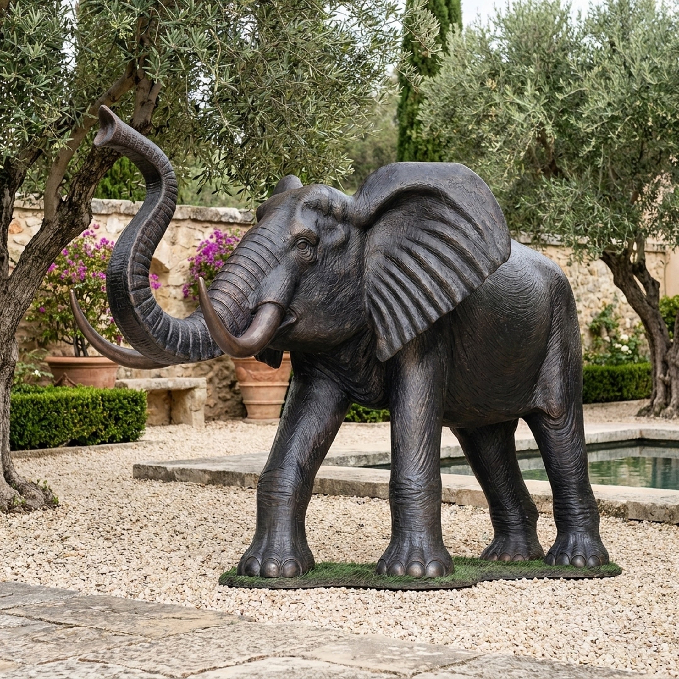 Monumental Traditional Standing Elephant Bronze Sculpture by Giant Sculptures with trunk raised, dark patina finish, displayed on gravel beside a garden pool.
