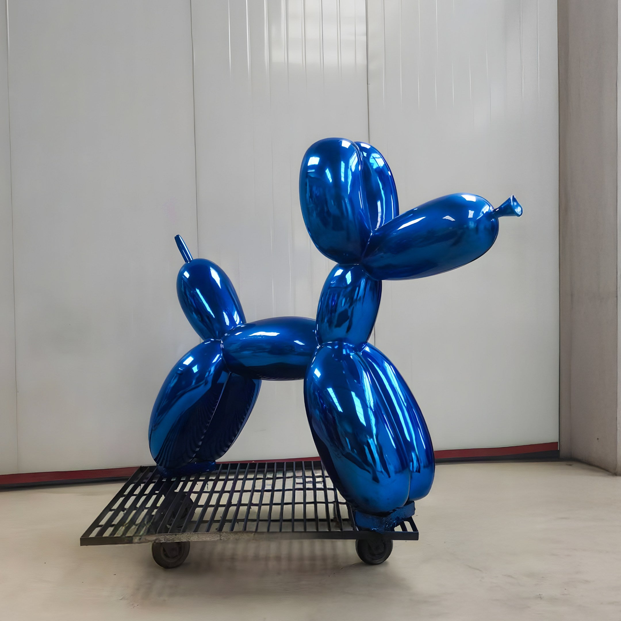 The Ocean Blue Balloon Dog Sculpture (80cm) by Giant Sculptures stands on a wheeled metal platform in a spacious room with white walls, epitomizing the clean aesthetics of modern interiors.