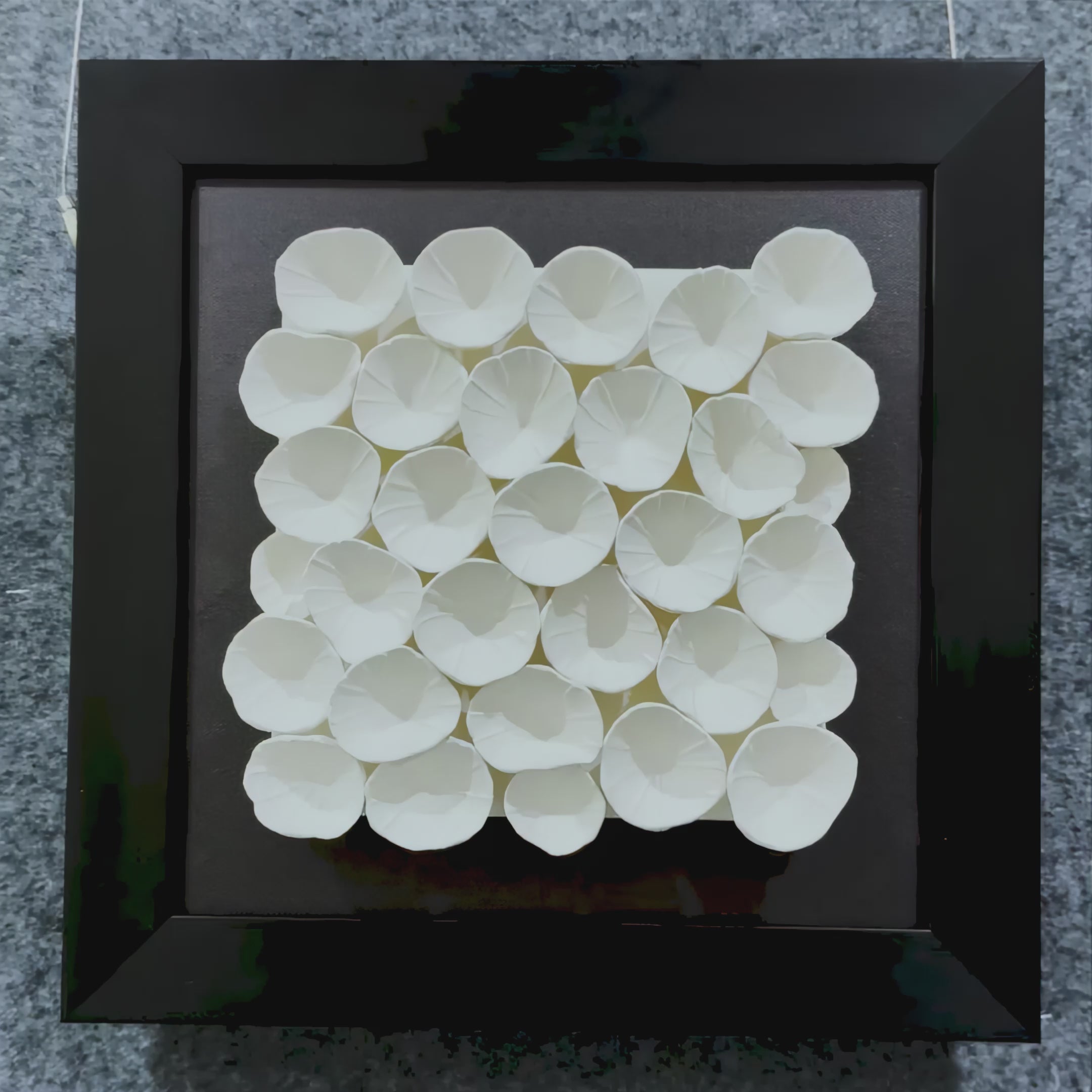 A visual tour of the Harmonia 3D Petal Wall Sculpture, showcasing delicately layered ceramic petals arranged in a floral cluster, set against dark fabric and enclosed in a black frame