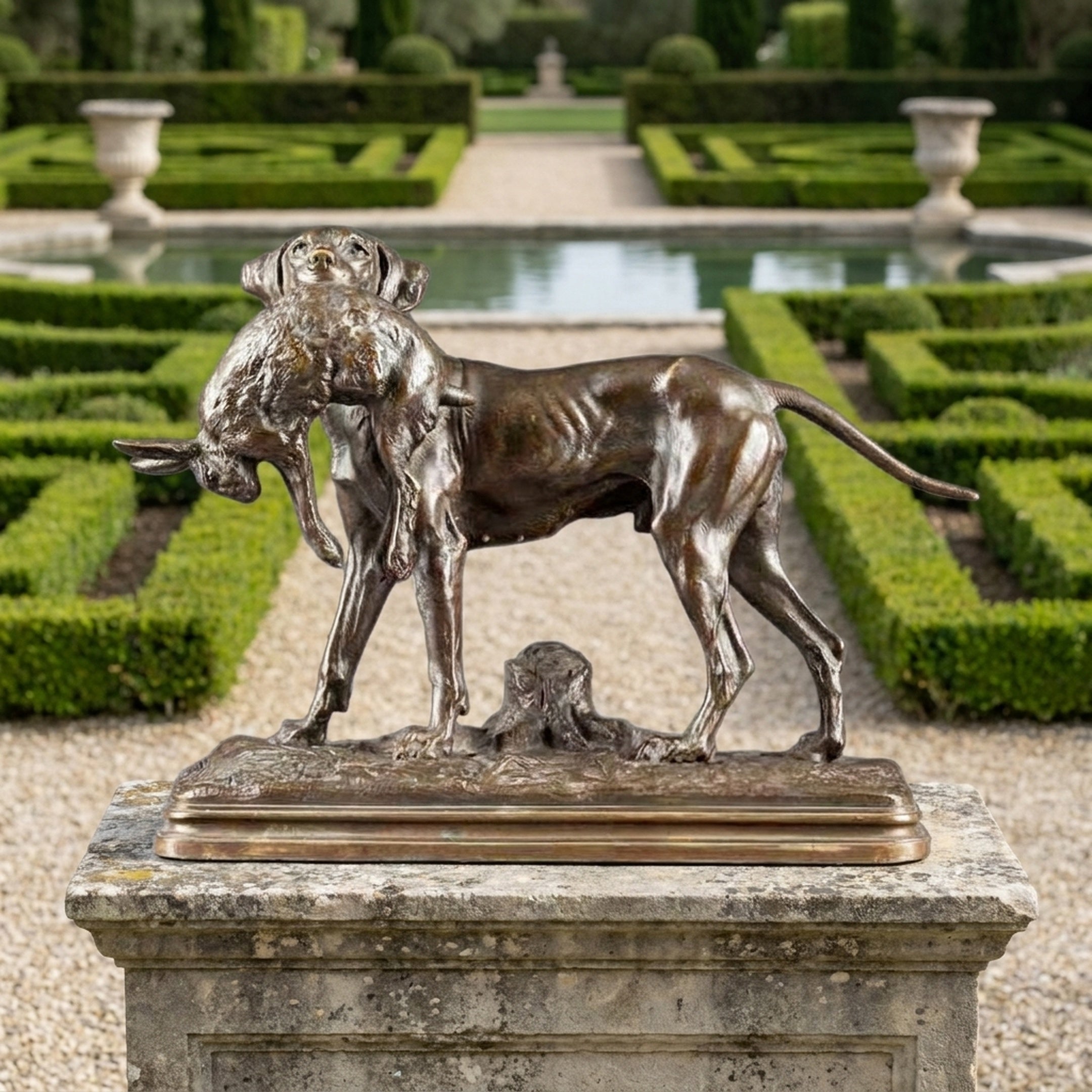 Traditional Hunting Dog with Hare Bronze Sculpture by Giant Sculptures displayed on a stone plinth in a formal garden with hedges and reflecting pool.