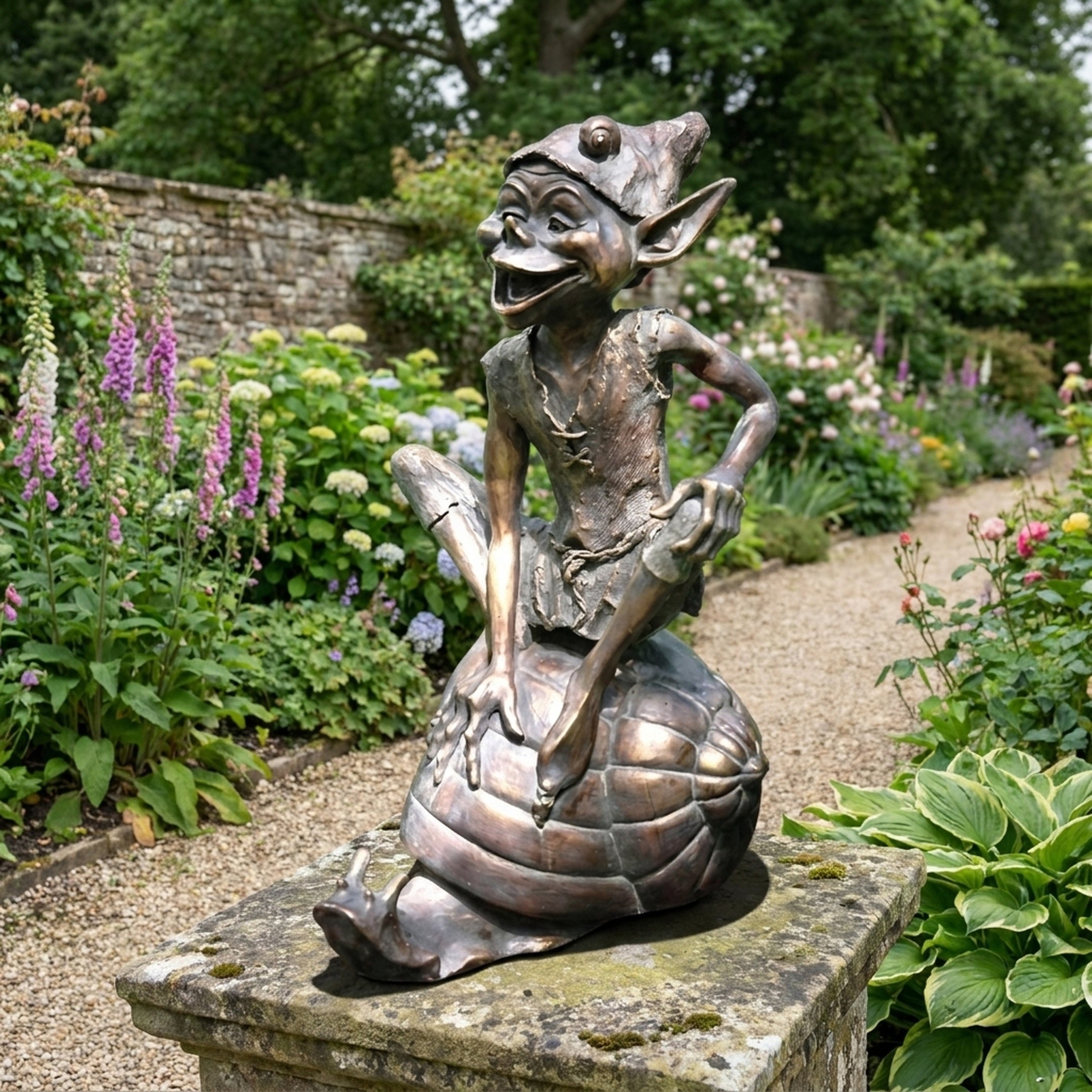 Traditional Laughing Goblin on Tortoise Bronze Sculpture by Giant Sculptures, warm brown patina, displayed on a stone plinth in a flower-filled garden path.