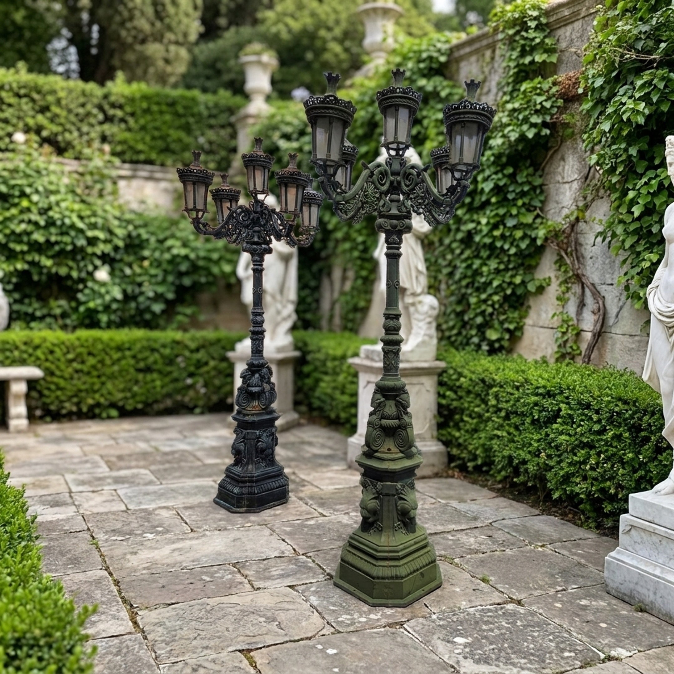Two Traditional Ornate Six-Arm Street Lamp Post Bronze Sculptures by Giant Sculptures on a stone courtyard, shown in black and verdigris green finishes.