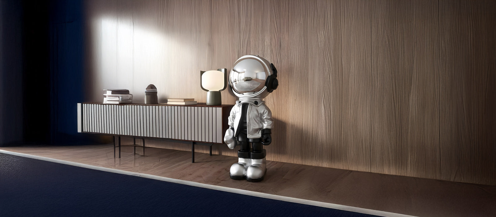 A shiny astronaut figurine stands on a wooden platform in a modern room, next to a sleek sideboard with books and a lamp. The background features a textured wooden wall.