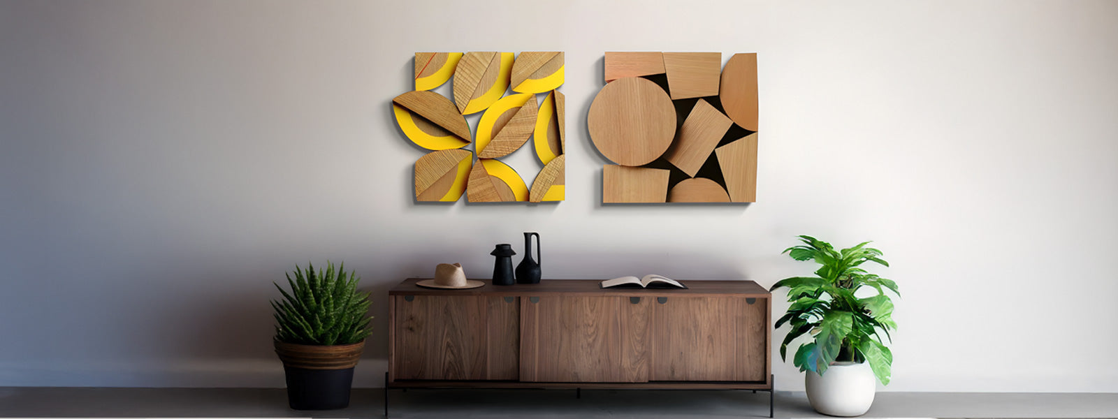 A modern living room features two abstract geometric art pieces on the wall above a wooden sideboard. The sideboard holds a small black vase and pot. Two plants flank the sideboard, adding greenery.