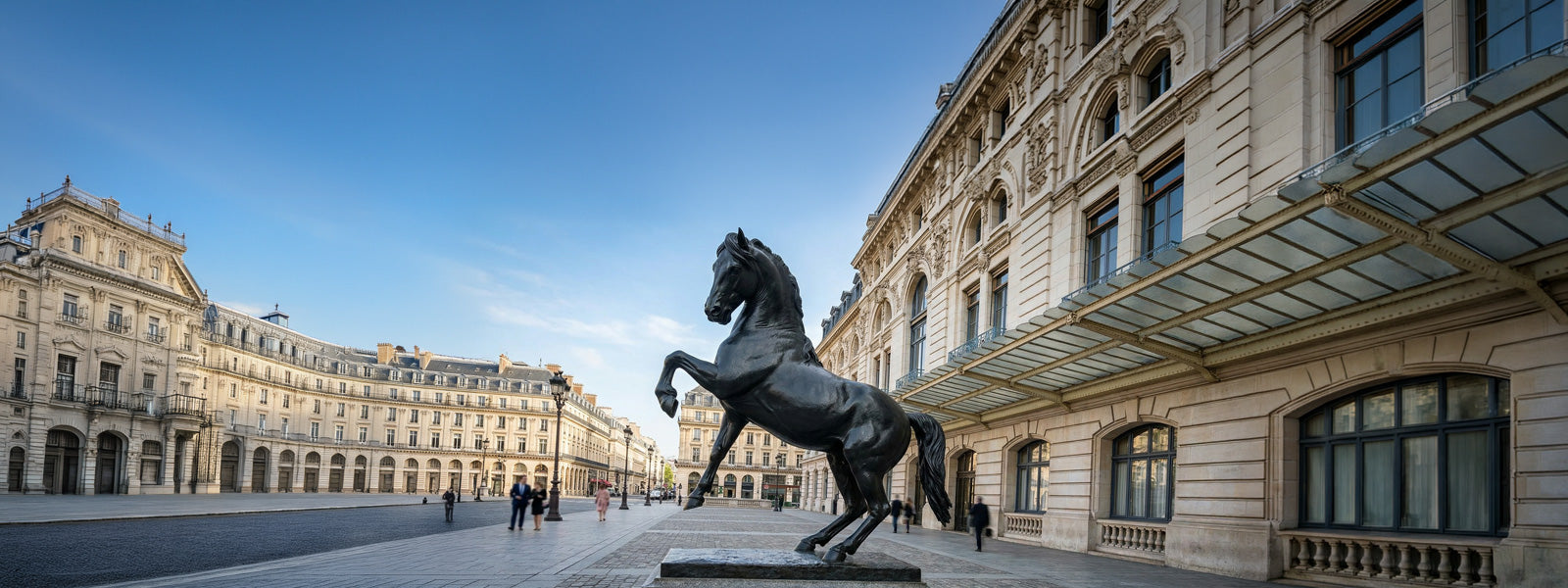 Large black rearing horse statue on a stone pedestal in a sunlit Parisian-style plaza surrounded by classical Haussmann-era buildings and pedestrians.