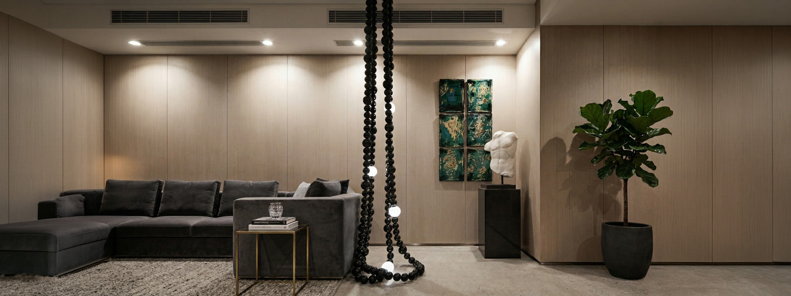 Modern living room with white torso sculpture on a dark pedestal, teal patina wall art, black beaded floor lamp, grey velvet sectional, and fiddle leaf fig.