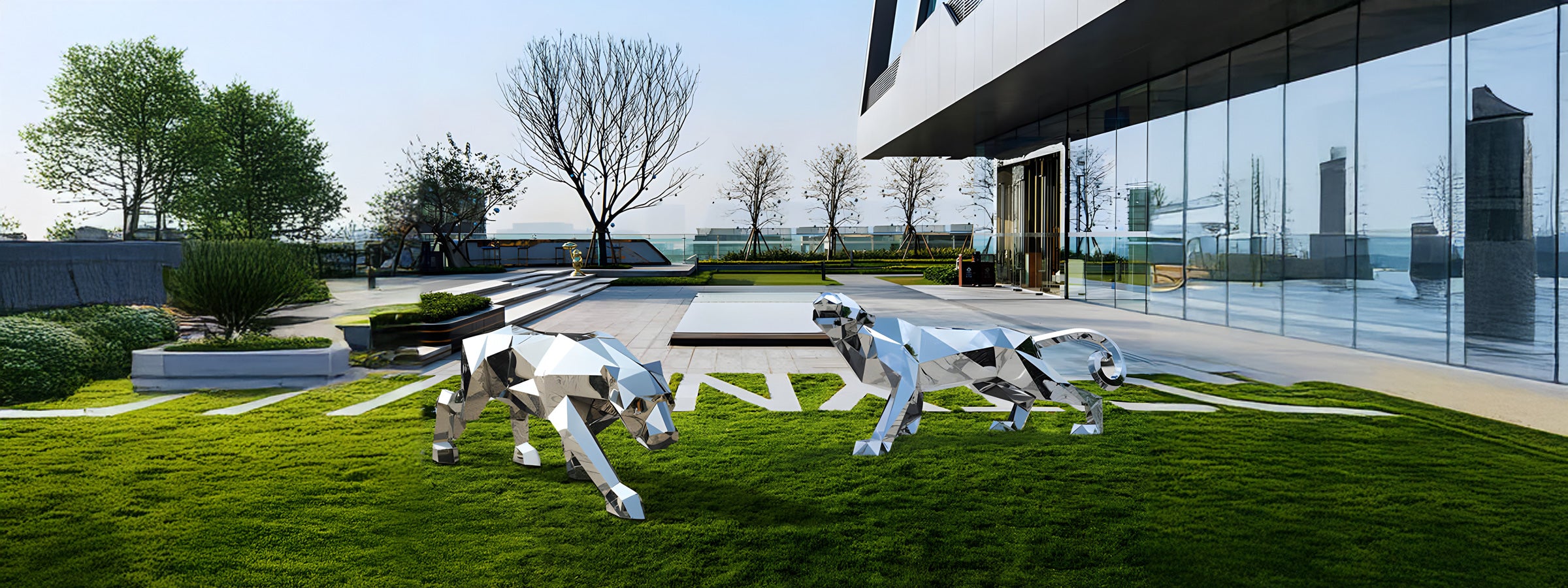 Two stainless steel geometric animal sculptures, a crouching panther and a walking monkey, displayed on a grassy area in a modern garden with minimalist architecture in the background.