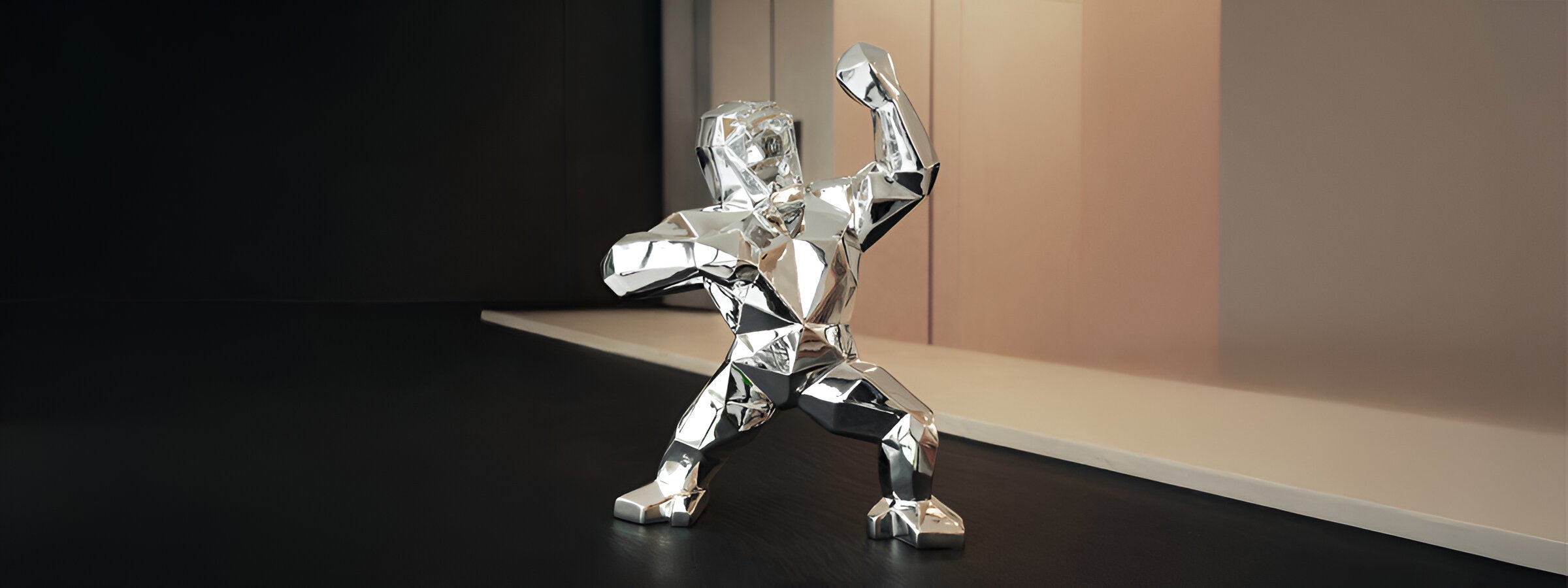 Shiny red geometric gorilla sculpture with angular, faceted design on a dark surface, posed with one arm raised. A woman in a black dress is blurred in the background, standing beside a large window.