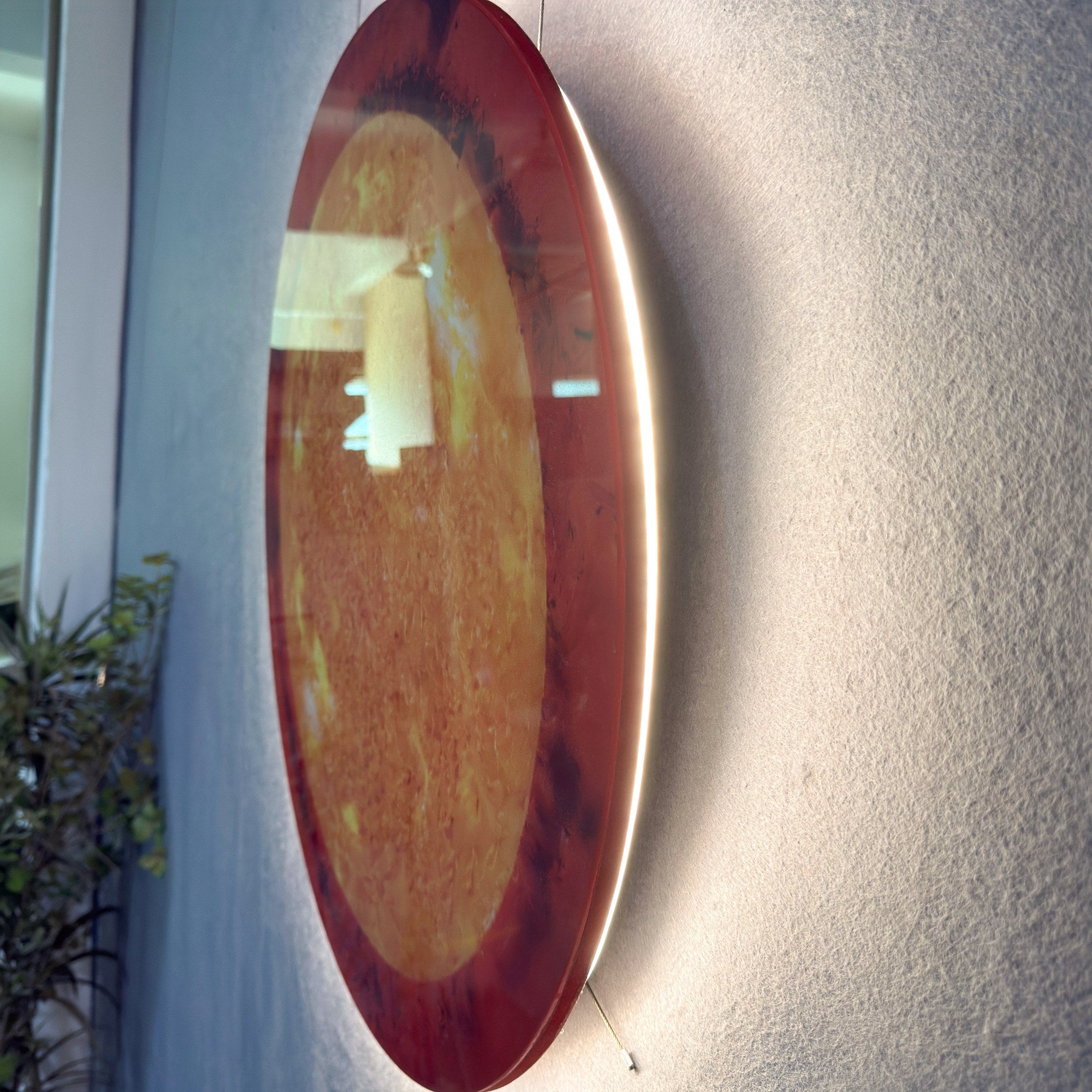 Galaxia Sun Crystal Porcelain LED Wall Art by Giant Sculptures viewed at an angle on a textured grey wall, showing its amber and golden marbled porcelain surface with concealed LED backglow illuminating the wall behind.