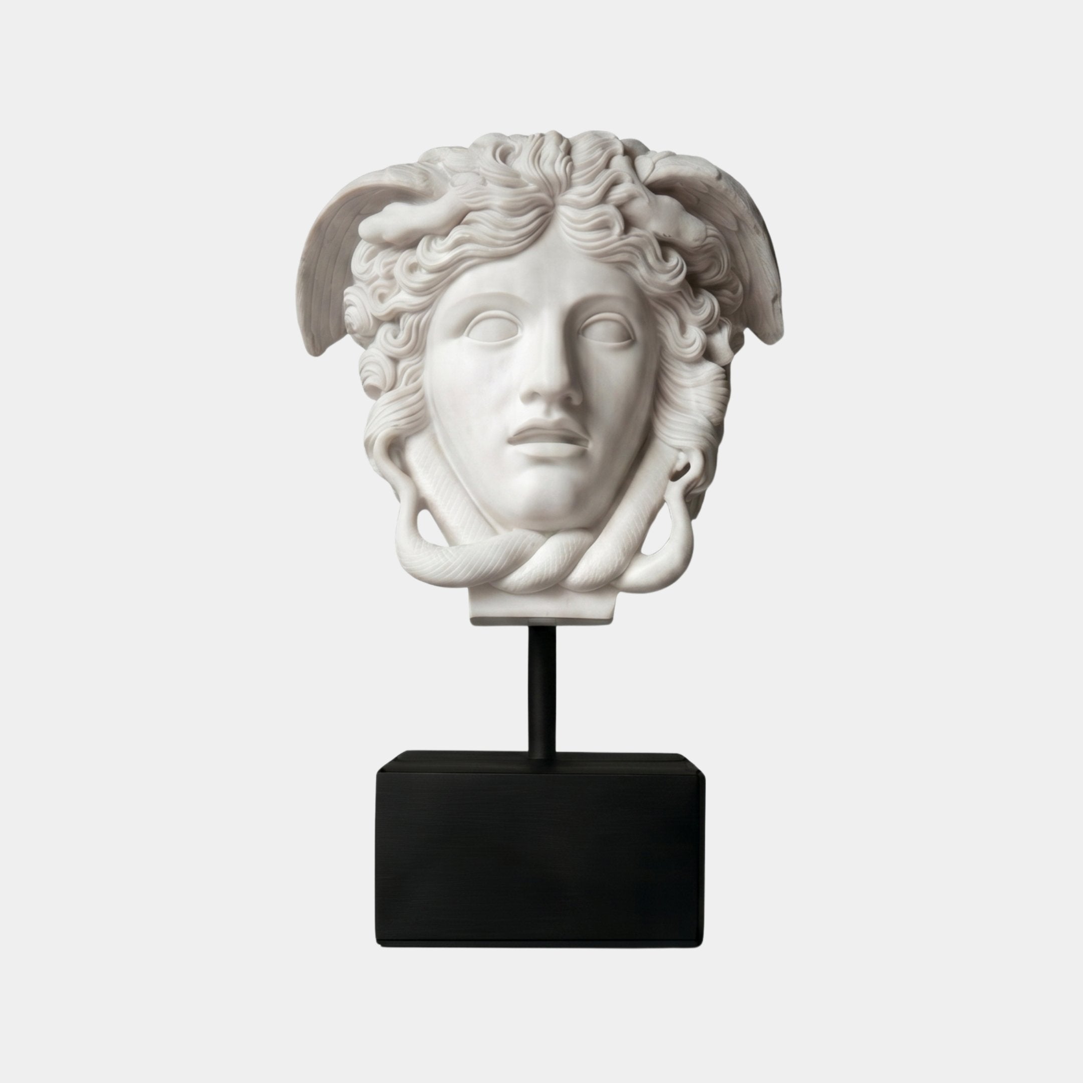 The Medusa Head Marble Sculpture - 80cm by Giant Sculptures features snake hair, wing details, and a calm expression on a black base. This elegant white sculpture stands out as a striking decor piece against a plain white background.