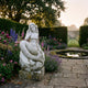 Giant Sculptures 80cm Mermaid Marble Sculpture seated on a rocky base beside a lily pond, surrounded by foxgloves, lavender, and roses in a hedged garden.