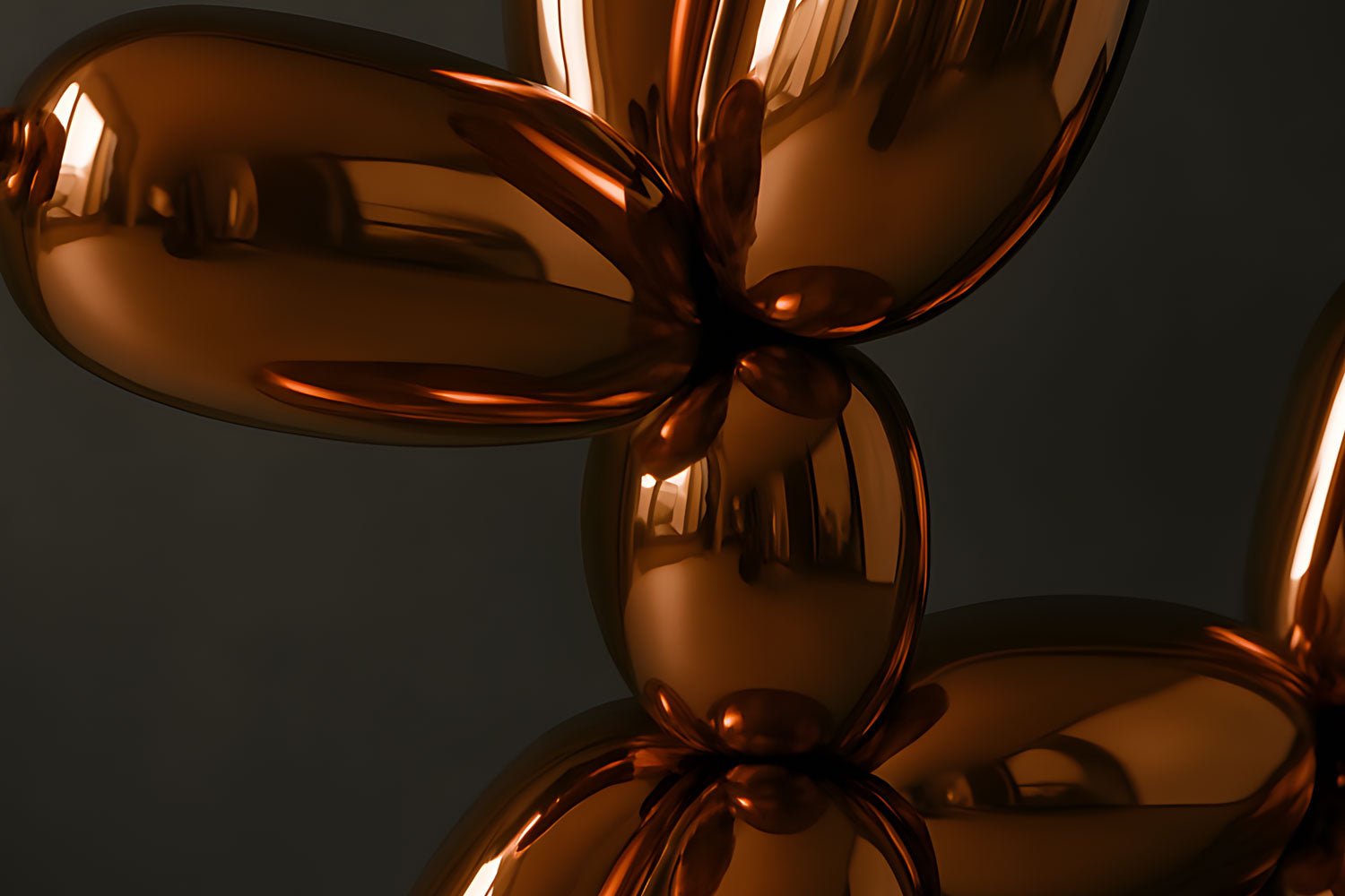 Close-up of a reflective, bronze-colored balloon sculpture with a shiny, smooth surface. The twisted shapes resemble parts of a balloon animal, set against a dark background.