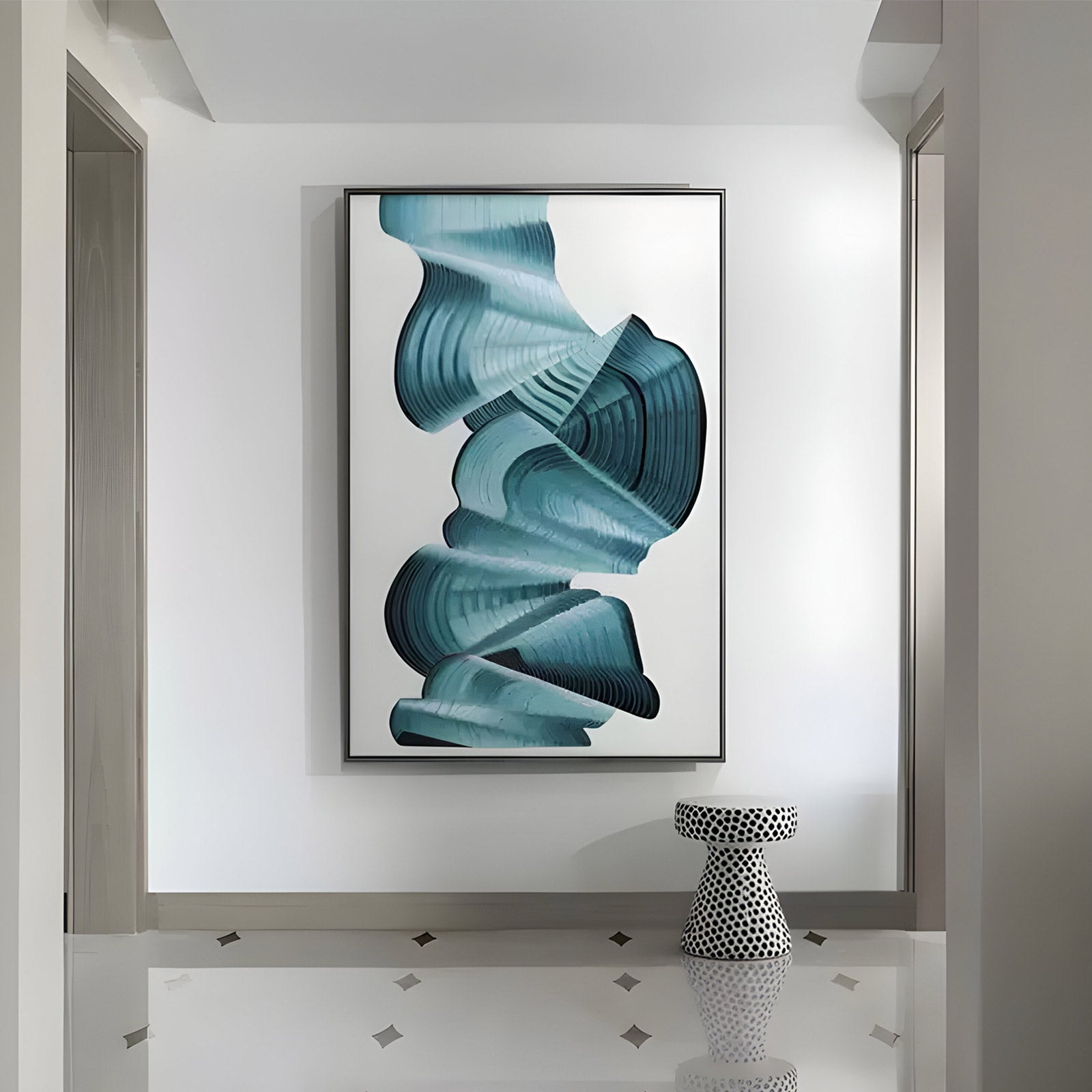 A large contemporary enamel painting featuring fluid, wave-like blue brushstrokes on a white background, framed in a sleek black border. The painting is mounted on a recessed wall in a modern interior, accompanied by a black and white polka-dotted stool on a tiled floor.