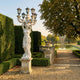 Giant Sculptures' 300cm Classical Woman Five-Arm Lamp Marble Sculpture on a pedestal beside a hedged garden path, with a reflecting pool and pavilion beyond.