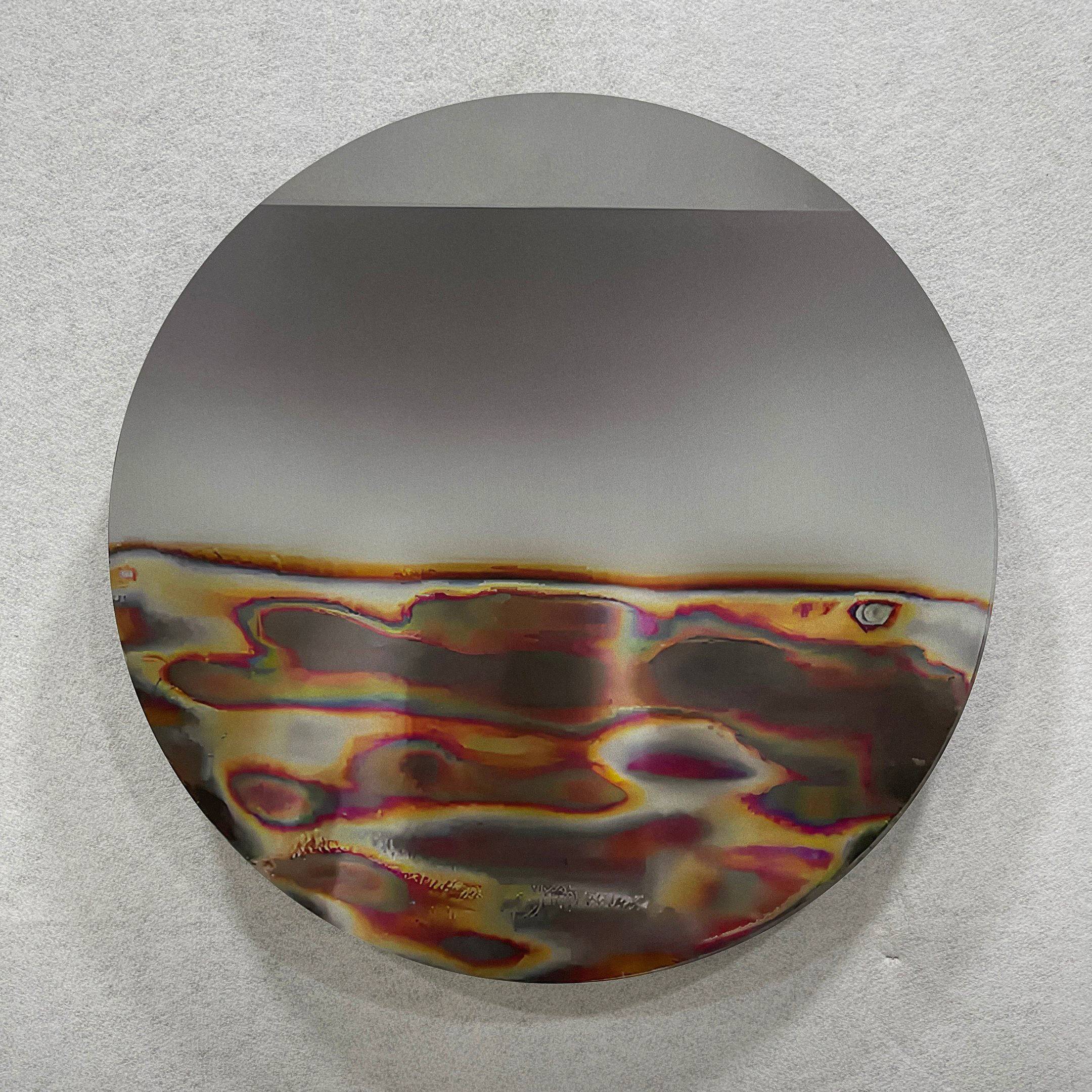 The Iridia Halo III Abstract Acrylic UV Wall Art by Giant Sculptures features a round metal disc with rainbow, bronze, and silver tones in an abstract pattern, evoking heat marks, set against a light gray background.