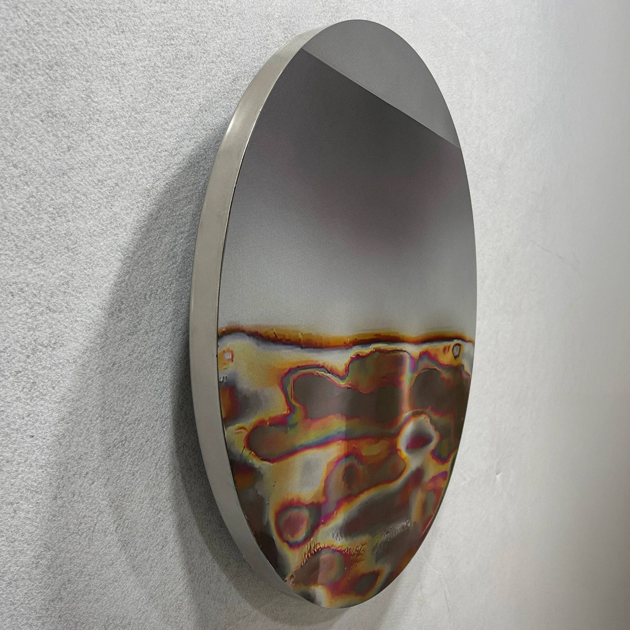 The Iridia Halo III Abstract Acrylic UV Wall Art by Giant Sculptures features a circular metallic design with a smooth, reflective finish. Iridescent red, orange, and purple waves flow on the bottom half; soft gray gradients complete the modern look above.
