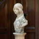 The Classical Maiden Marble Bust - 60cm by Giant Sculptures depicts a serene woman in a headscarf with downcast eyes, displayed on a decorative pedestal against dark wooden panels.