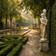 Classical Woman Lamp Marble Sculpture 180cm by Giant Sculptures on a stone pedestal beside a formal hedged garden with reflecting pool at golden hour.