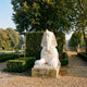 Giant Sculptures Egyptian Sphinx Marble Sculpture 110cm in white marble with nemes headdress, displayed on a stone plinth in a formal garden with hedges.