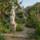 Giant Sculptures 180cm Standing Female Figure marble sculpture on a weathered stone plinth in a cottage garden with roses, wildflowers, and an apple tree.