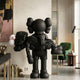 Obsidian Black Iconify Rescuing Furry Sculpture by Giant Sculptures, 135cm matte black figure cradling a limp furry companion, displayed in a neutral living room.